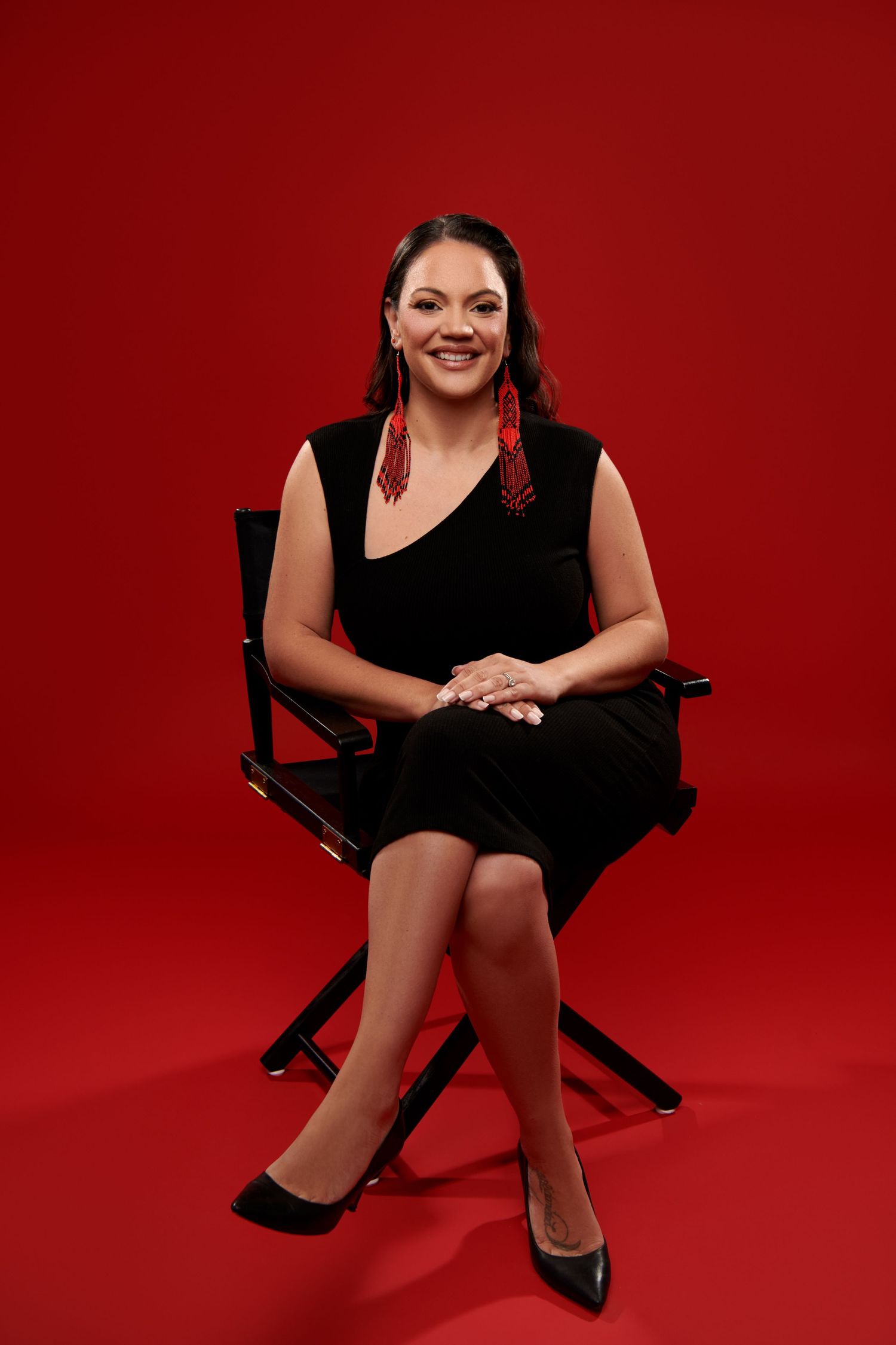 A person in a black sleeveless dress poses against a red background with hands resting on a white surface. Gricel's Photography New Jersey