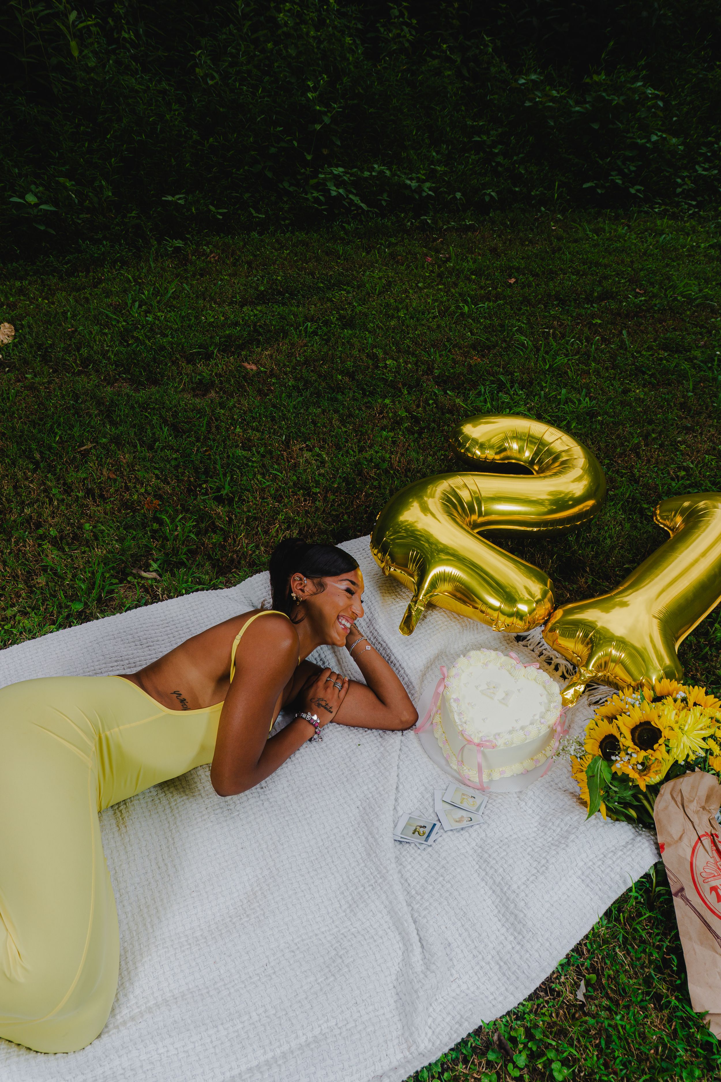 Outdoor photo series with gold number balloons, sunflowers, and yellow dress on white blanket.