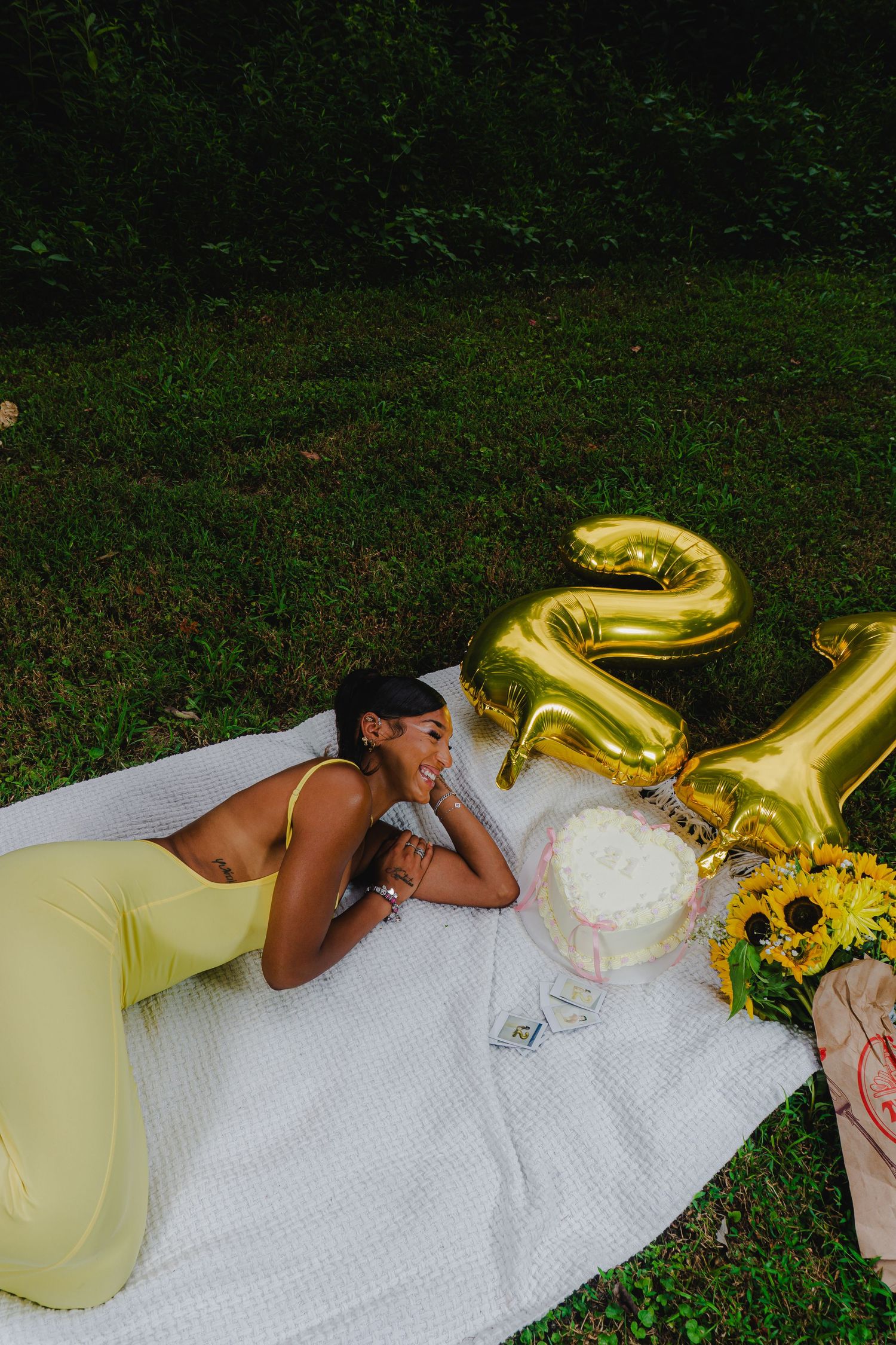 Outdoor photo series with gold number balloons, sunflowers, and yellow dress on white blanket.