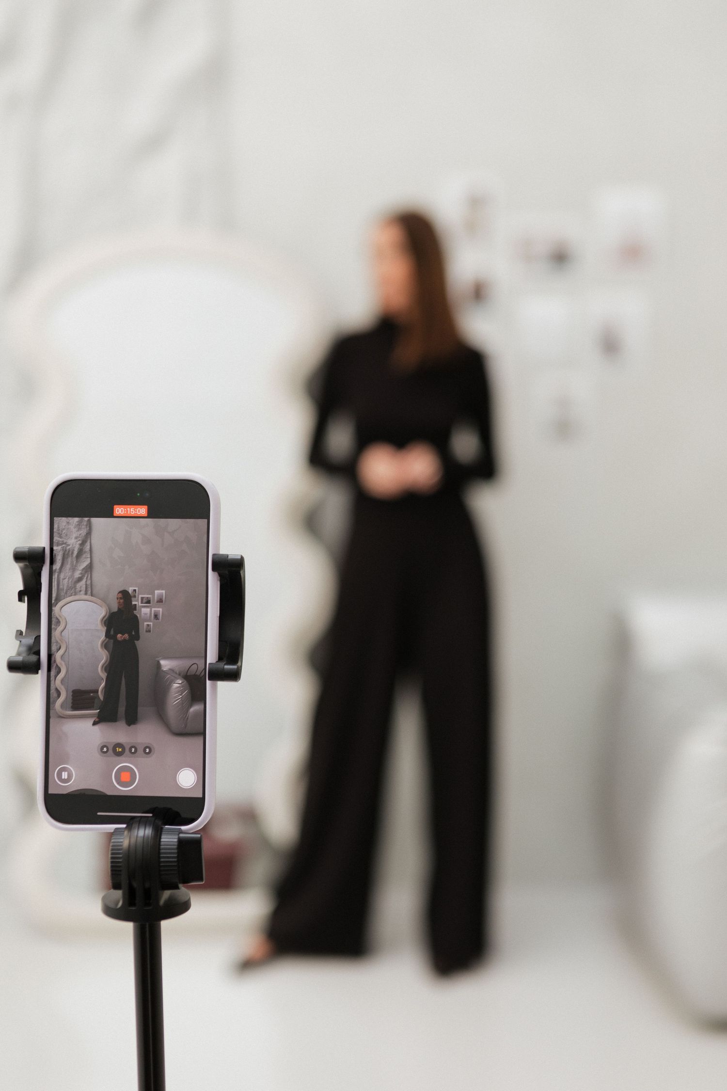 Mobile phone mounted on a tripod stand with blurred figures in a white studio background. For branding shoot & content.