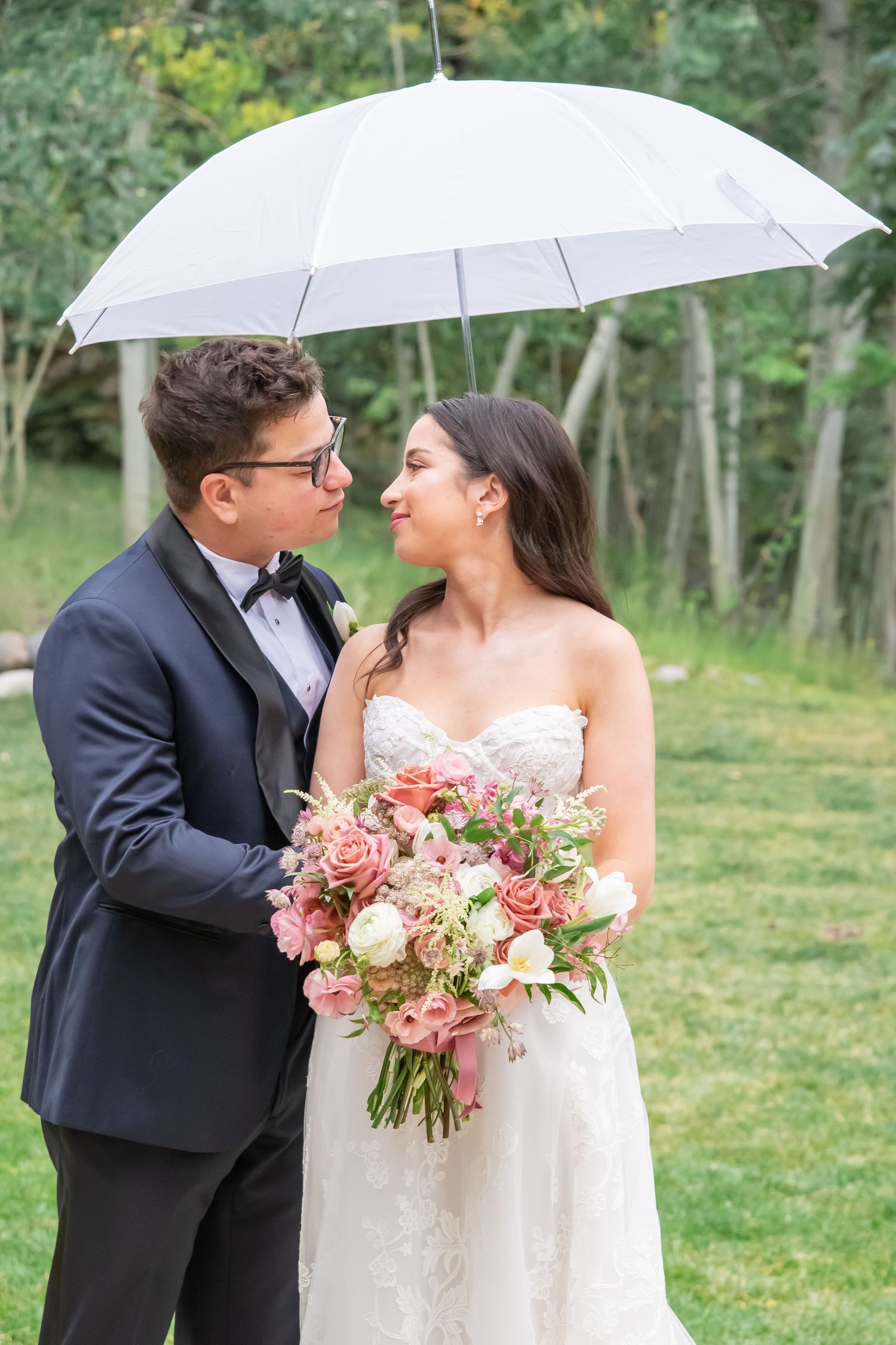 Romantic wedding photos under white umbrella with pink bouquet and natural greenery backdrop.