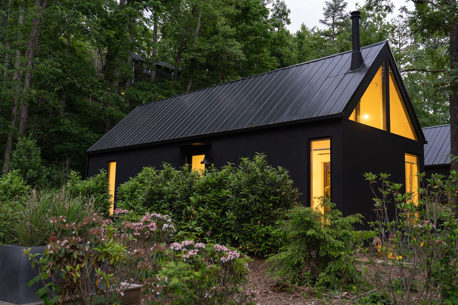 One of Firelight at Shope Creek's cabins lit up in the evening in late spring, with rhododendron bushes in bloom in the foreground