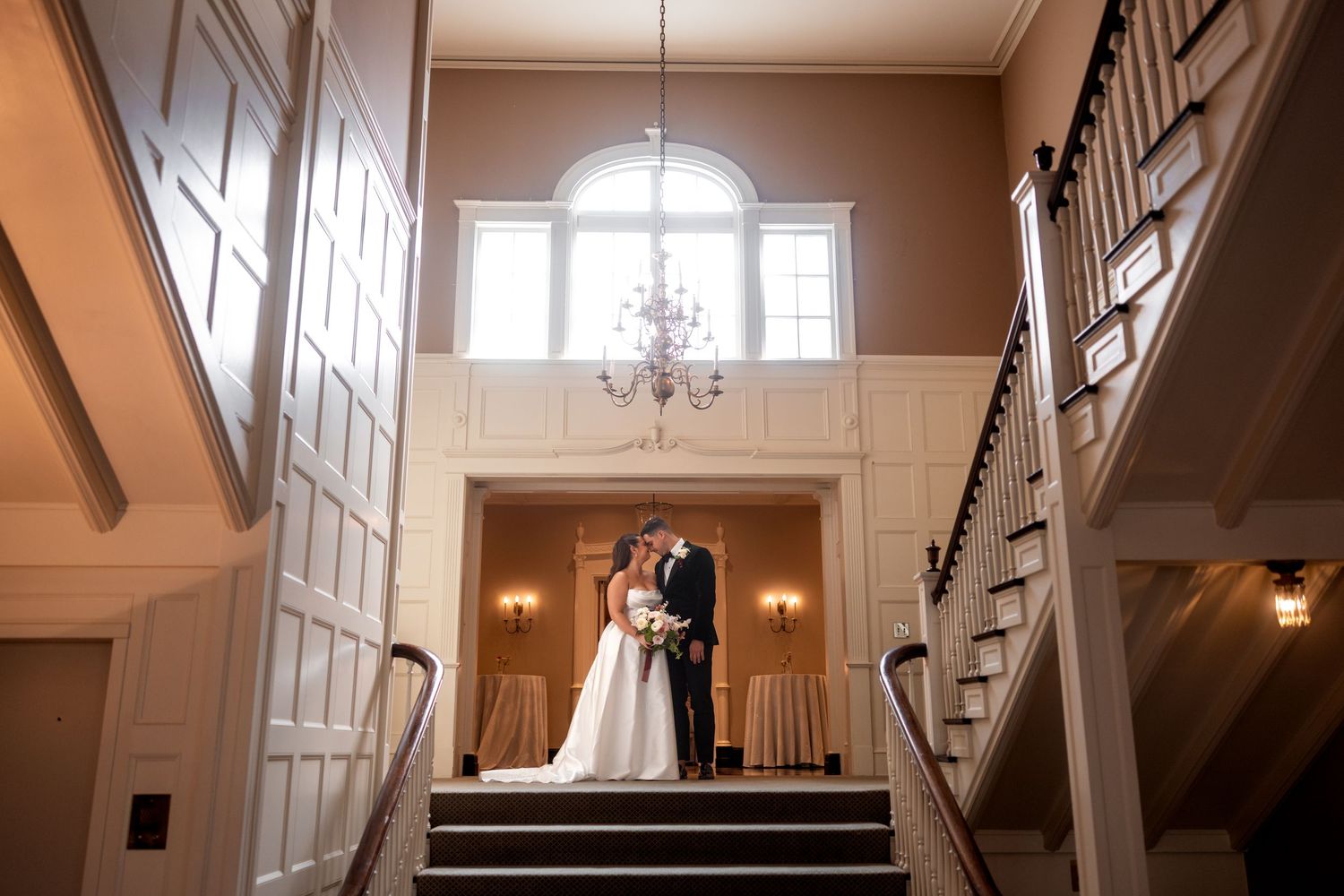 Elegant white staircase with ornate wainscoting and wall panels in a traditional foyer illuminated by warm sconces.