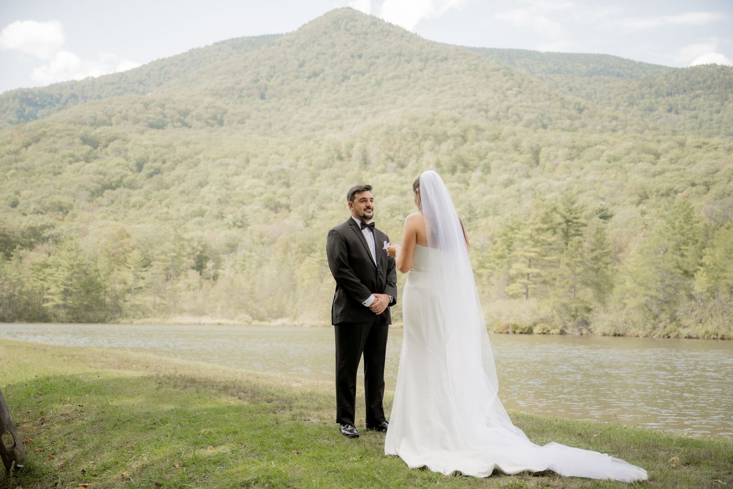 Two people share a tender moment against a mountainous backdrop at an outdoor wedding ceremony.