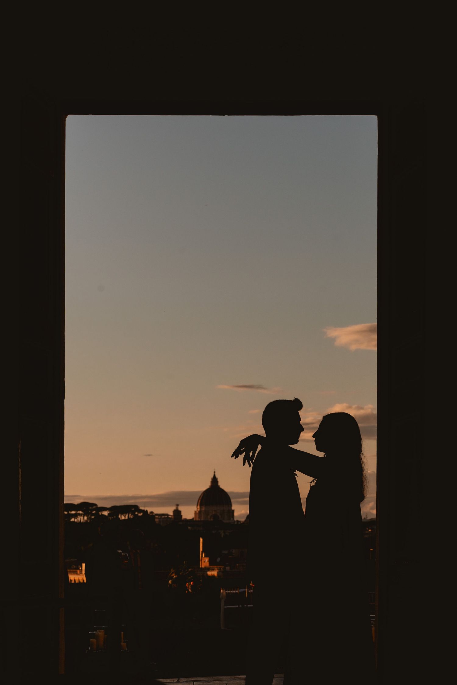 Silhouettes of buildings and figures against a dramatic sunset sky in Rome.