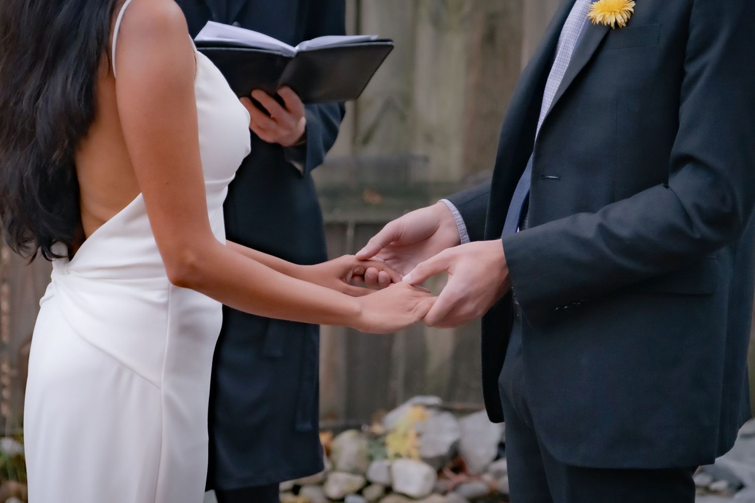 A bride and groom hold hands during an outdoor wedding ceremony as guests look on.