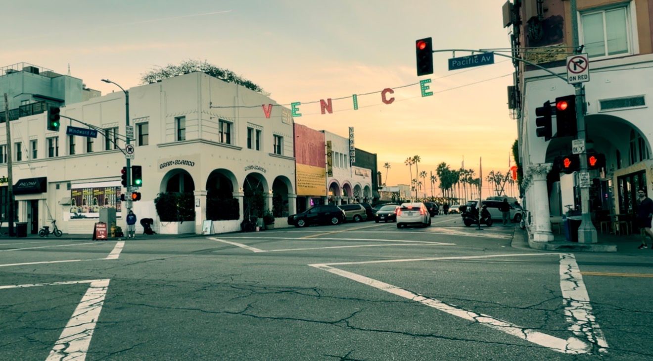 A panoramic urban street view with storefronts and buildings during golden hour lighting.
