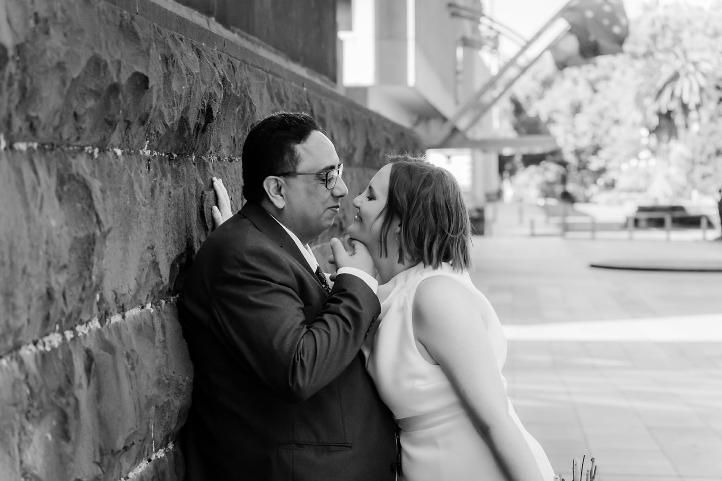 Black and white photography series showing a romantic couple sharing intimate moments against a stone wall.