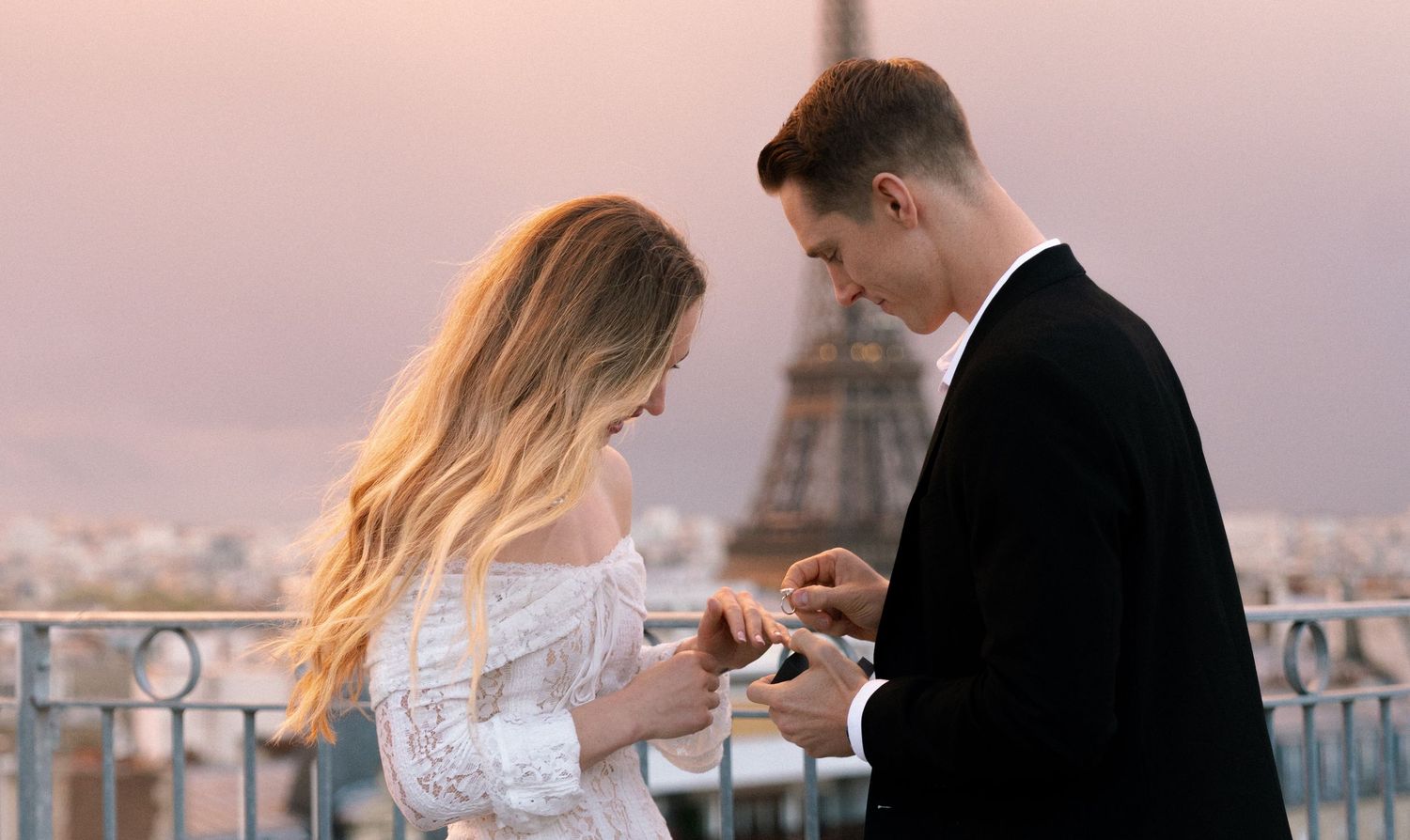 Silhouetted couple shares intimate moment on rooftop balcony during sunset with city skyline in background.
