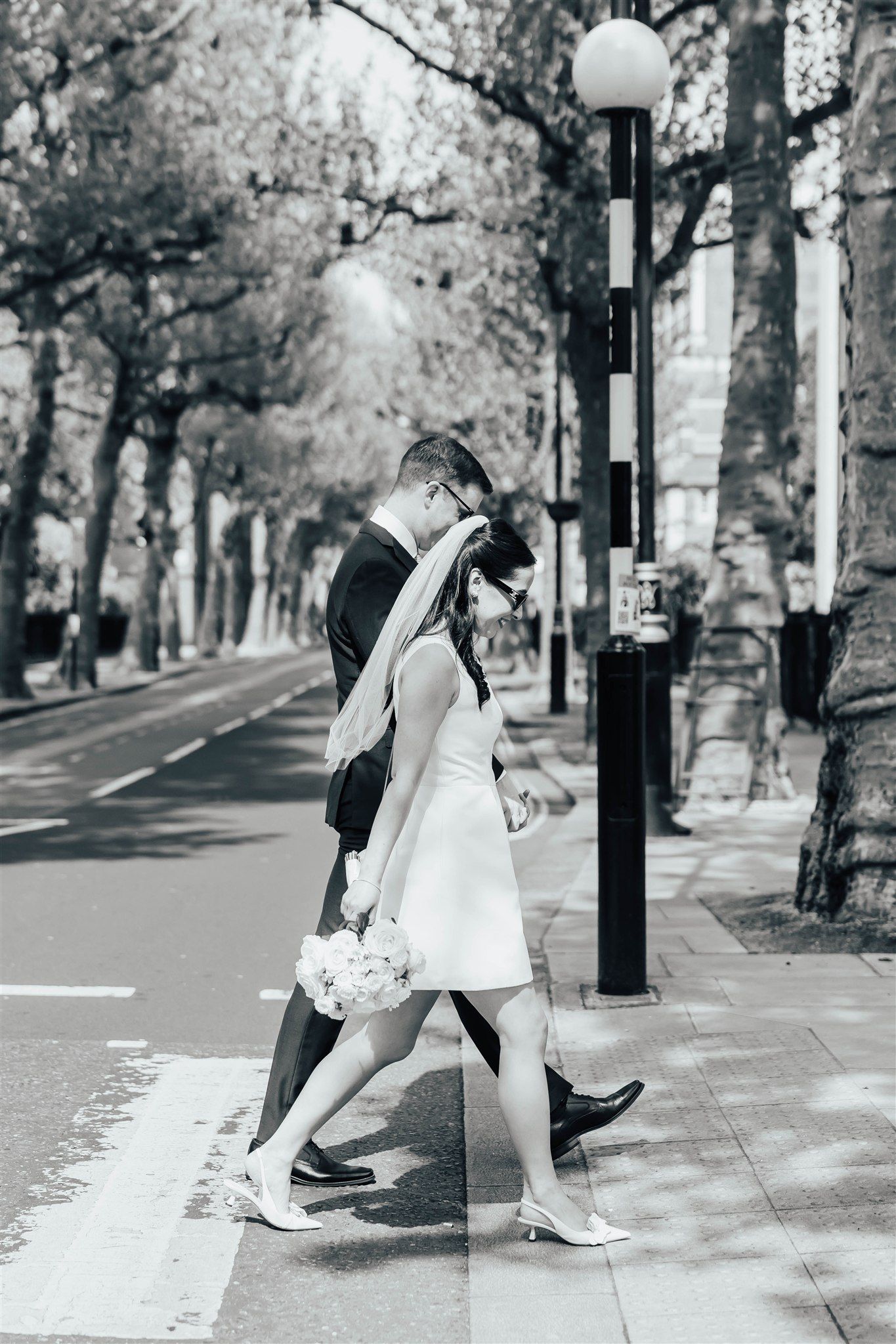 A series of black and white photos showing a wedding couple in a short white dress walking along a tree-lined street in central London.