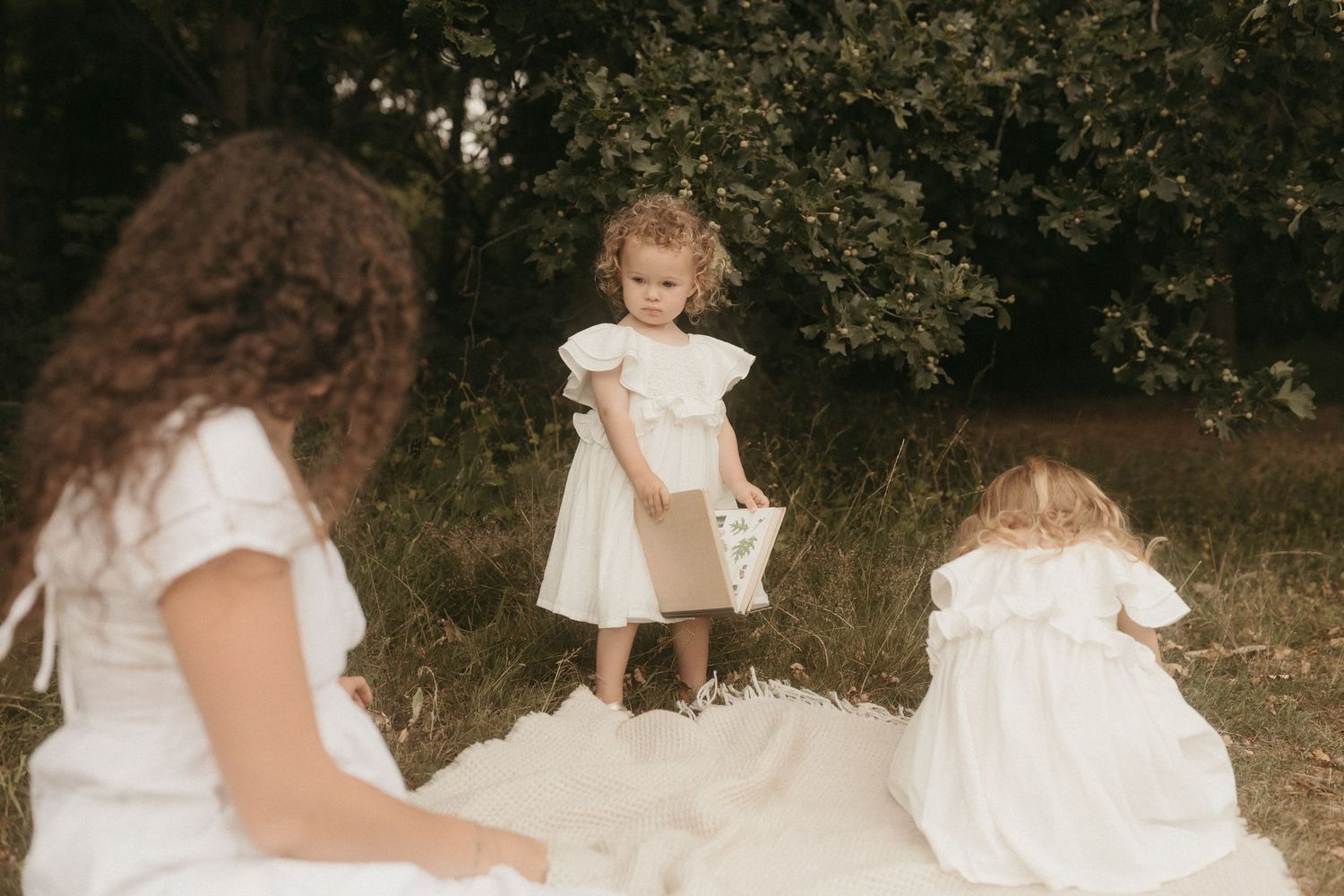 Children in vintage white dresses play together outdoors in a garden setting with a dreamy retro aesthetic.