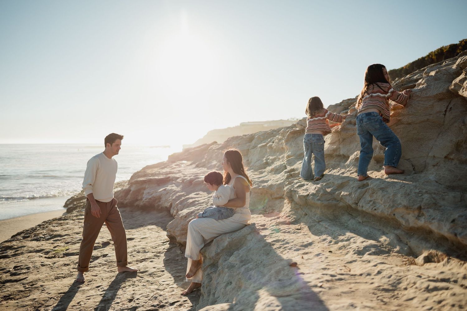 People enjoying a sunny day climbing on coastal rocks at the beach during golden hour.