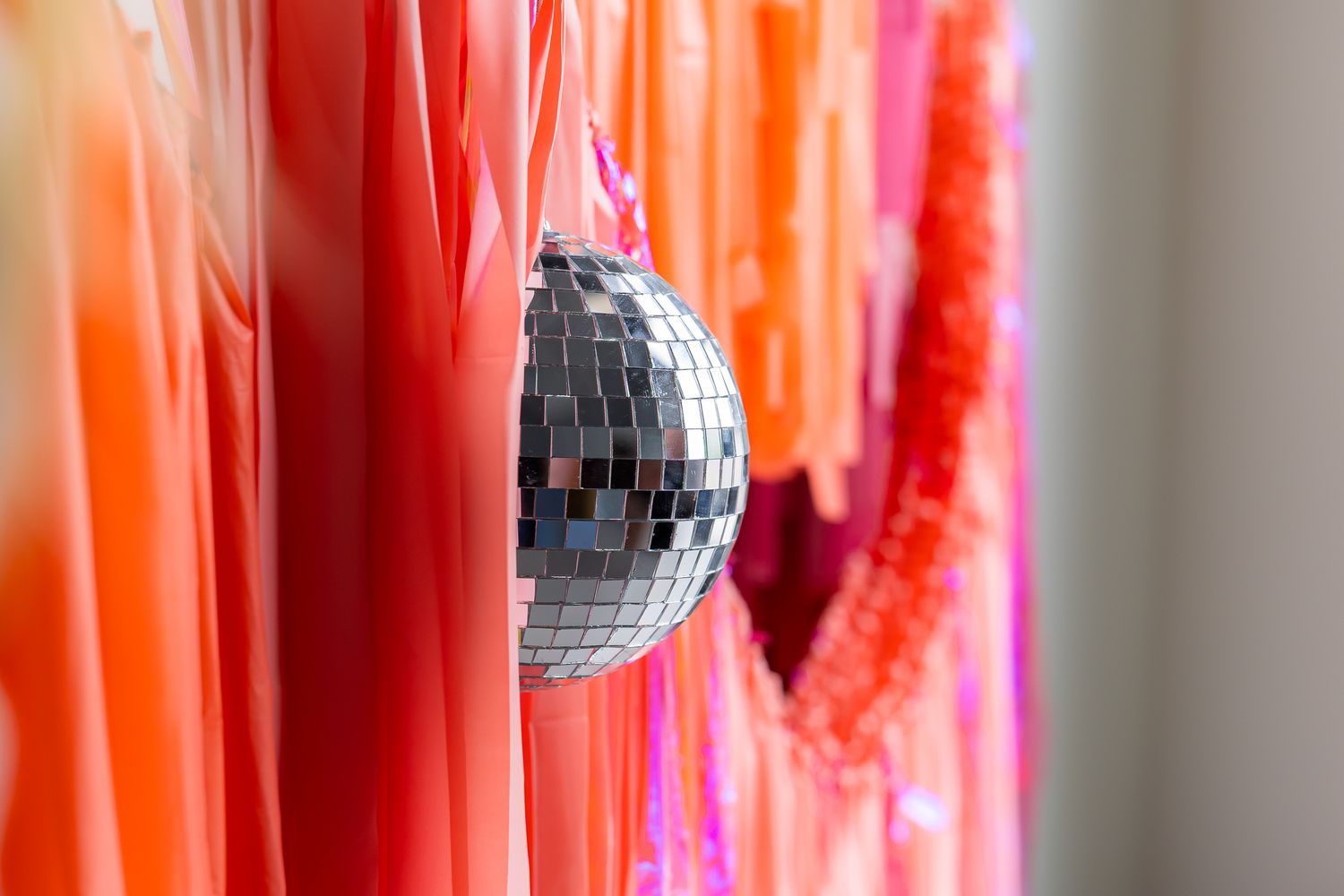 Disco ball hangs with pink & orange fringe backdrop for party company's branding photoshoot by photographer in Pittsburg, KS and Joplin, MO.