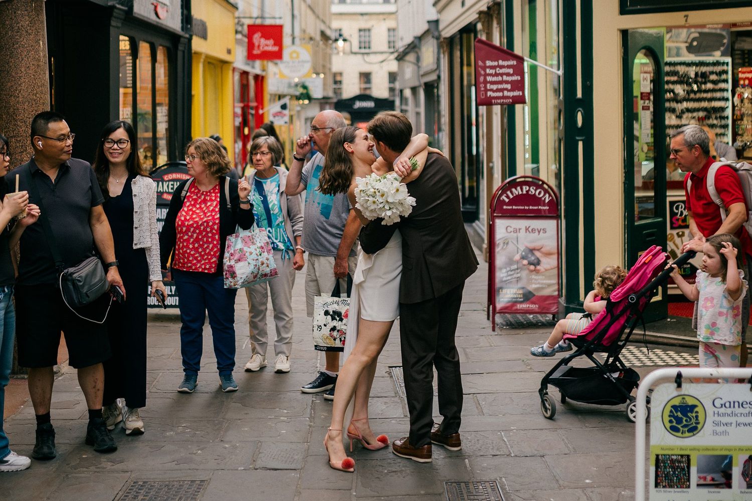 People walking and shopping on a busy pedestrian street lined with retail stores during an elopement wedding in Bath, UK.