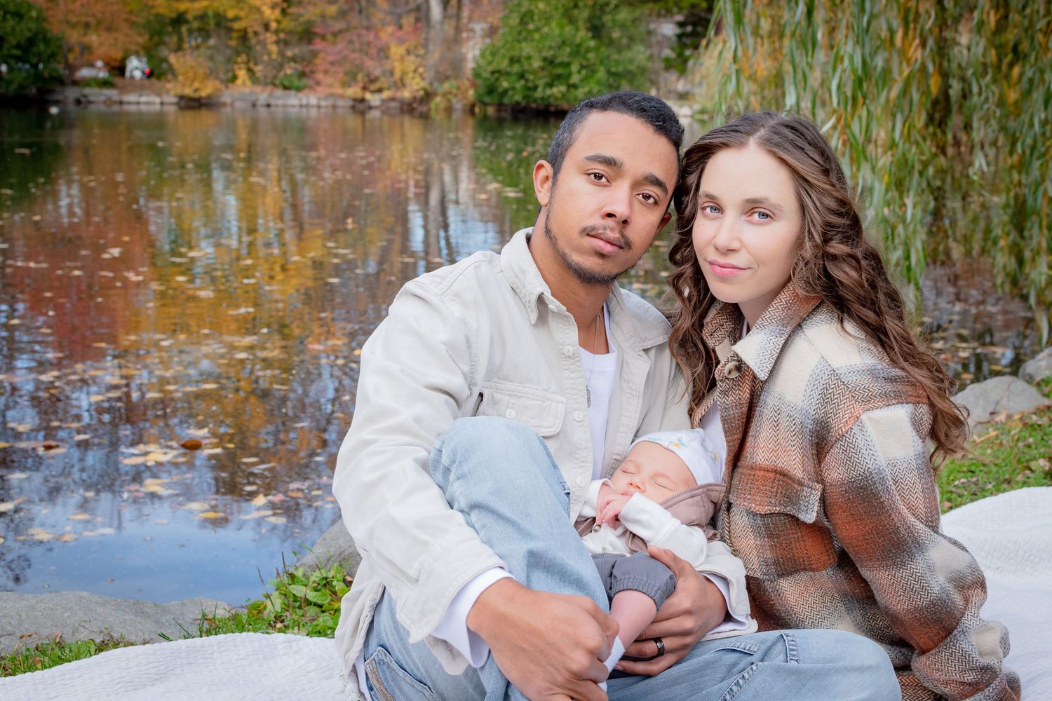 Family sitting together during fall newborn photo session at Wright Park in Tacoma with colorful autumn leaves behind them.