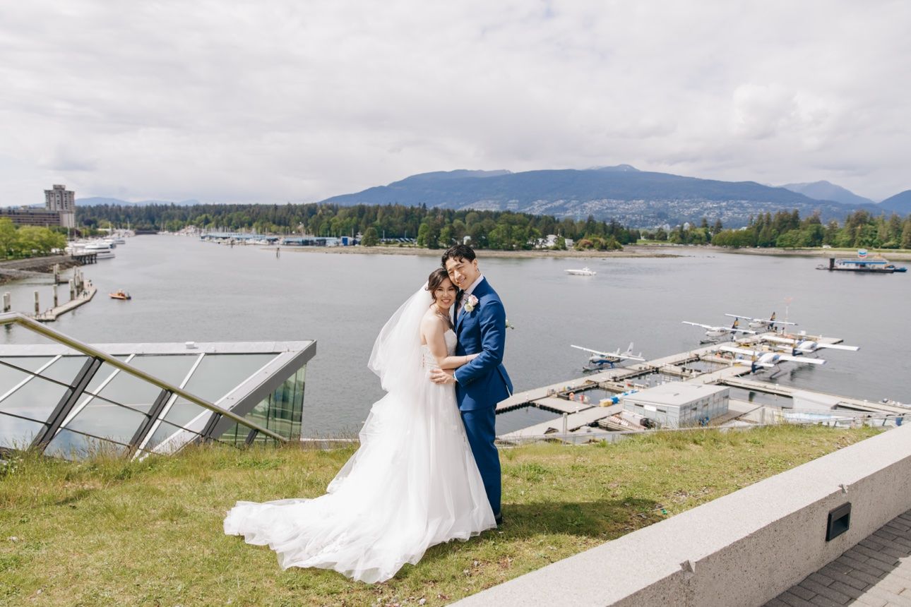 Bride and groom embracing above Coal Harbour with Stanley Park and North Shore mountains behind them, Vancouver luxury wedding photography