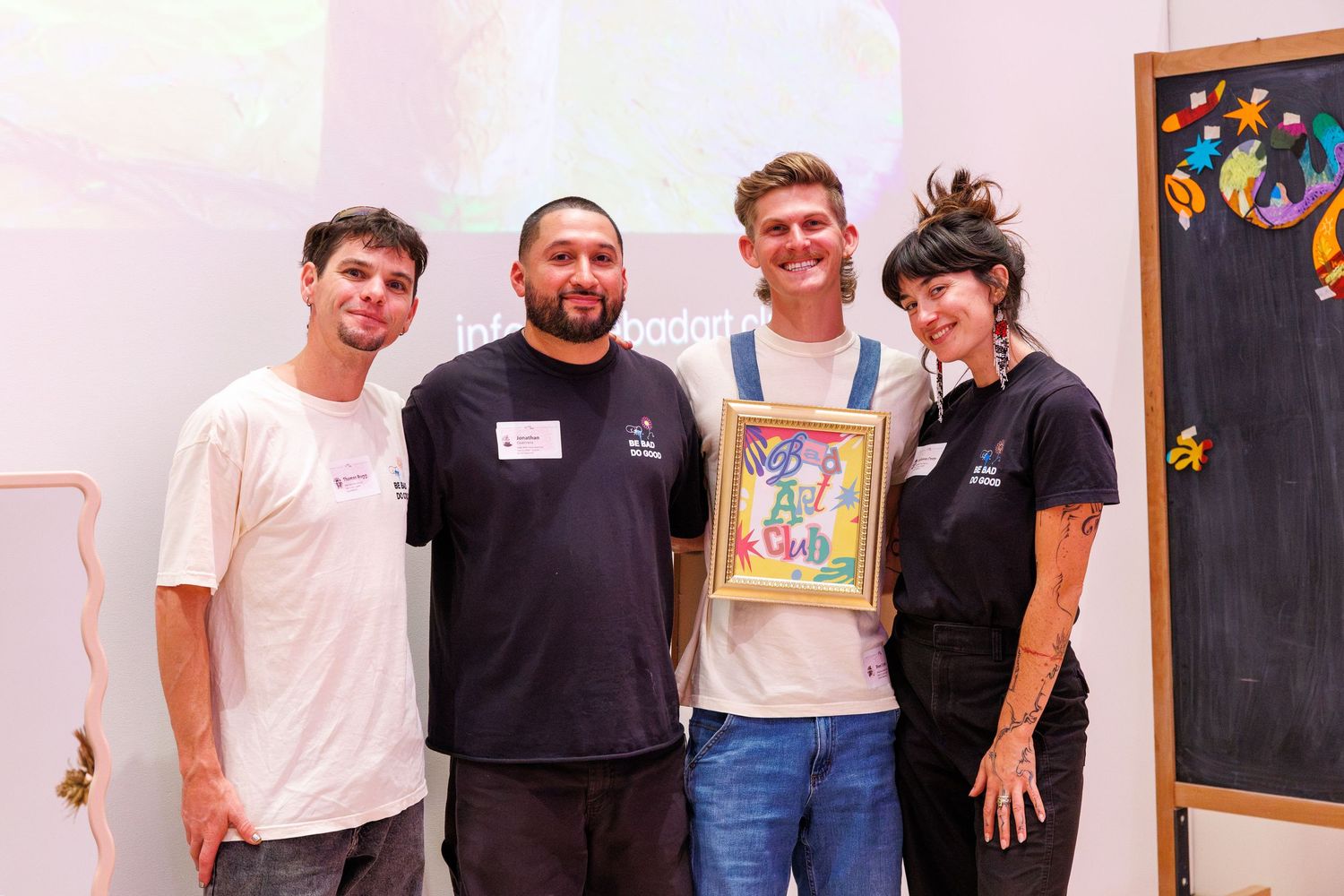 Four people smiling and posing together holding a colorful framed artwork at an indoor event.