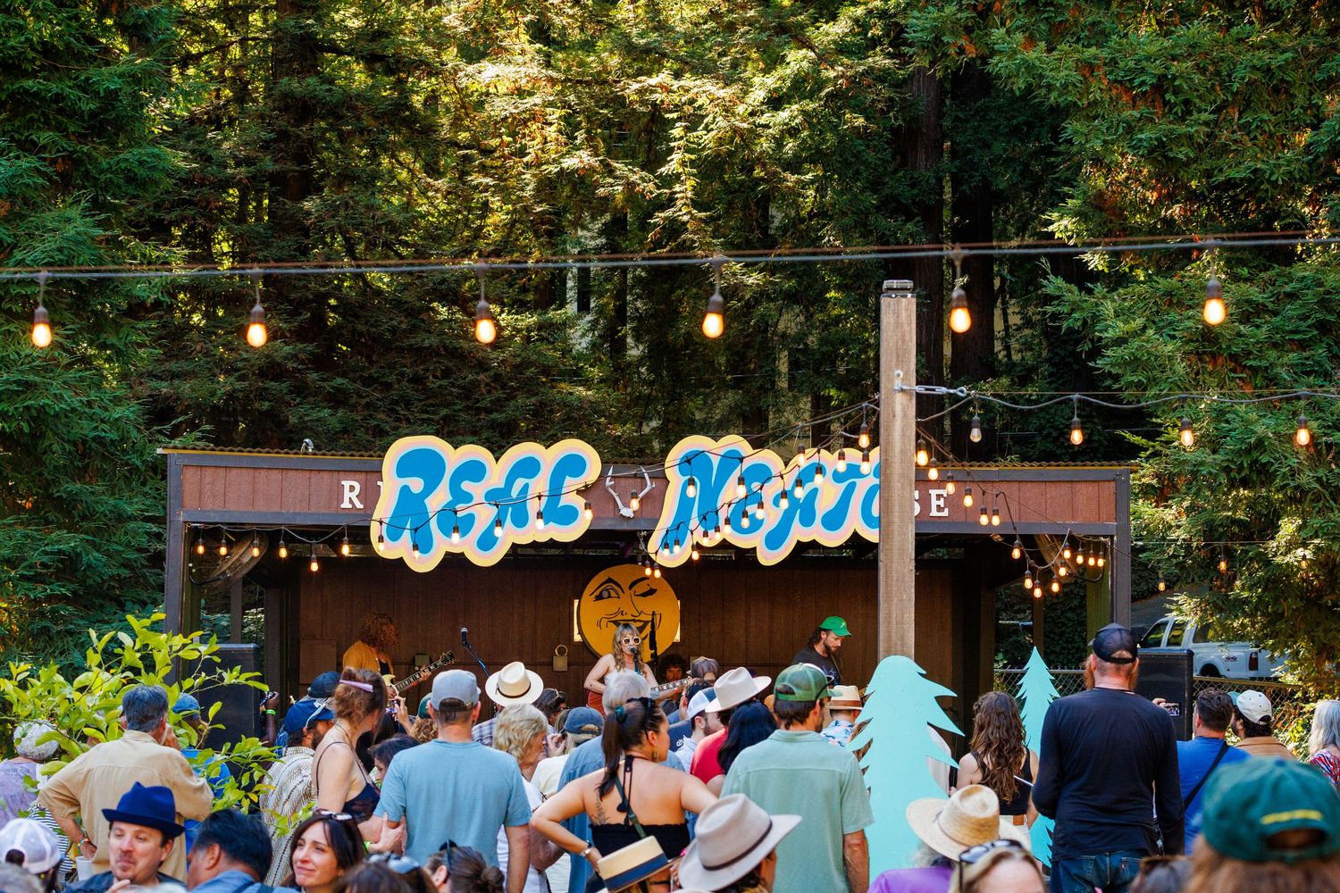 Outdoor stage decorated with colorful paper trees and a smiling moon backdrop displaying the band name Real Neato.