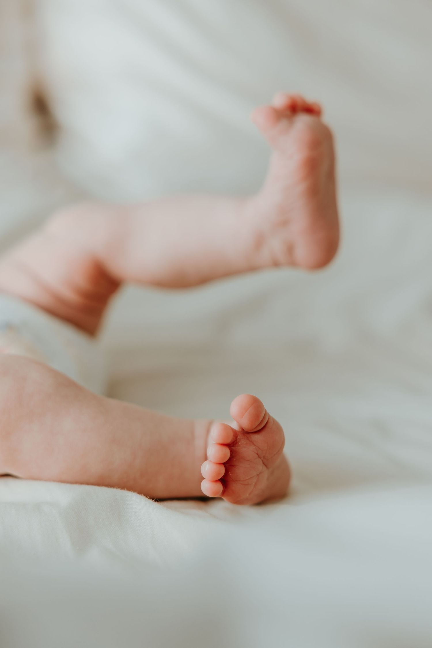Four closeup photos of tiny newborn baby feet resting on soft white bedding in a tender photoshoot.