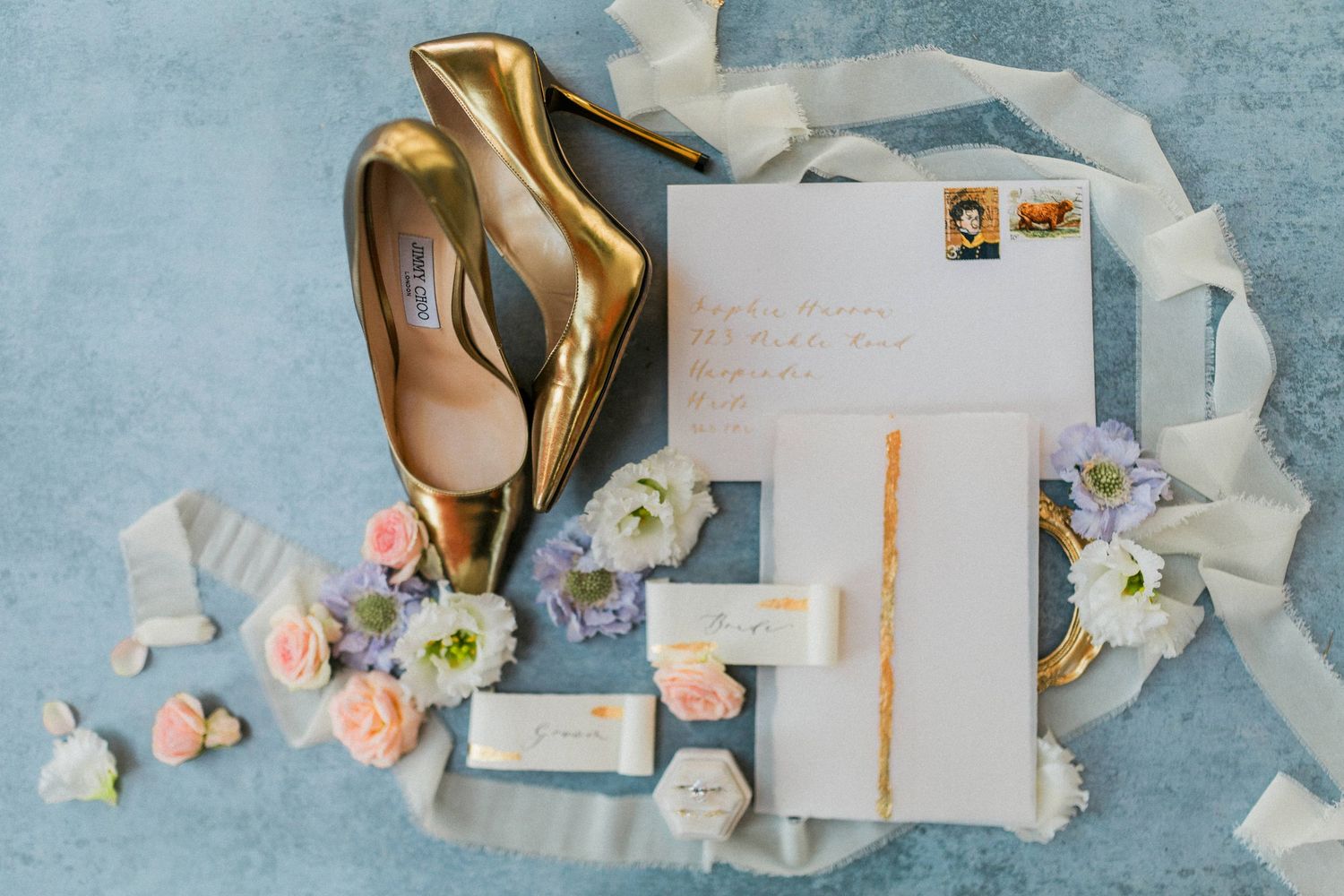 Wedding invitation flatlay with Jimmy Choo shoes and pastel flowers on a light blue background with delicate silk ribbons at Euridge
