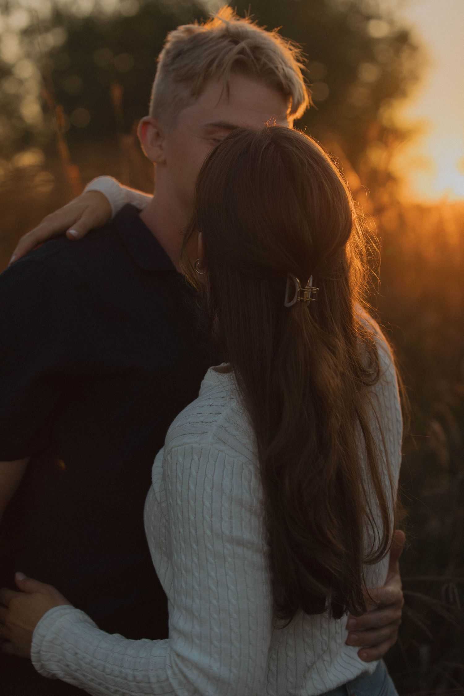 An intimate couple embraces during golden hour sunset in cozy winter sweaters.