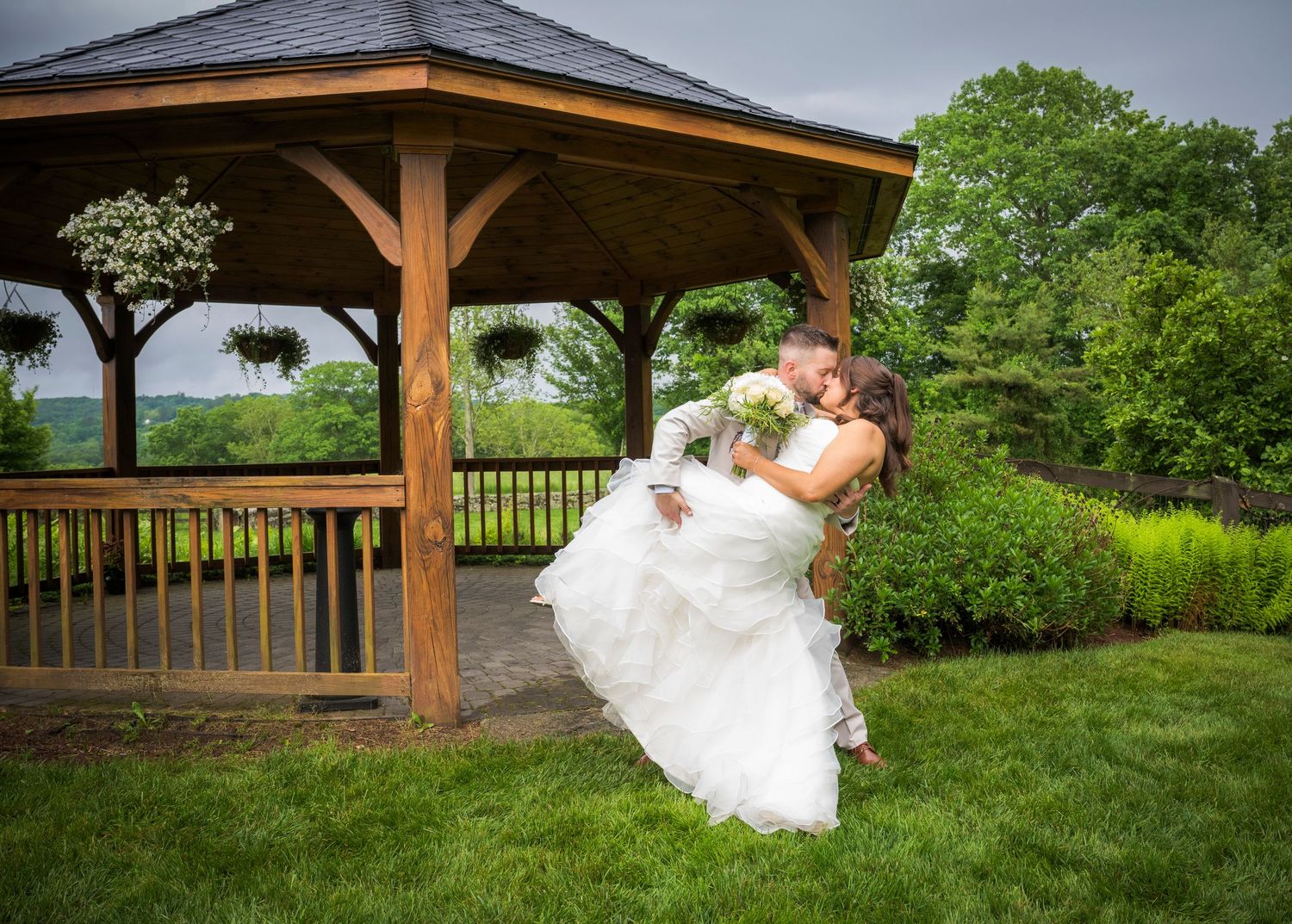 Newlyweds share an intimate moment outdoors with autumn foliage and rustic architecture in background.