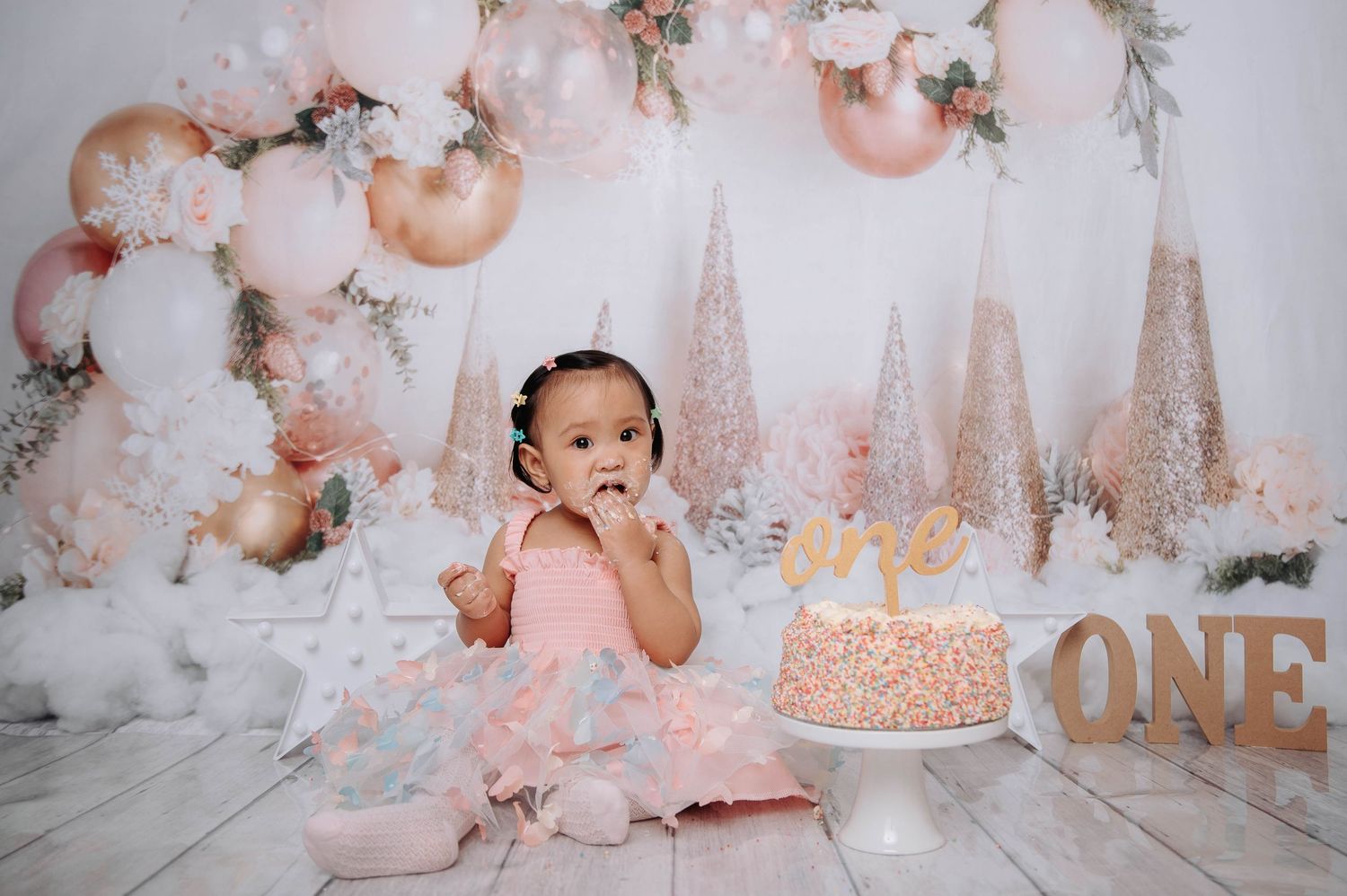 Elegant first birthday setup with pink balloons, cake, and winter wonderland decorations on white background.