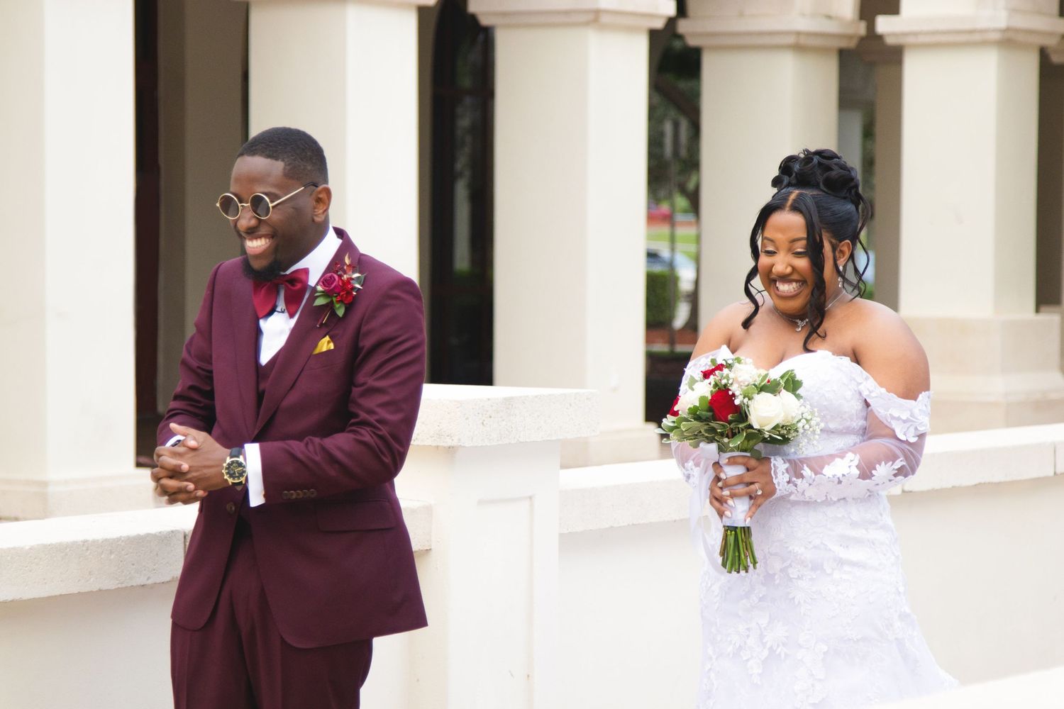 First look wedding moment with bride in white dress holding bouquet and groom in burgundy suit.