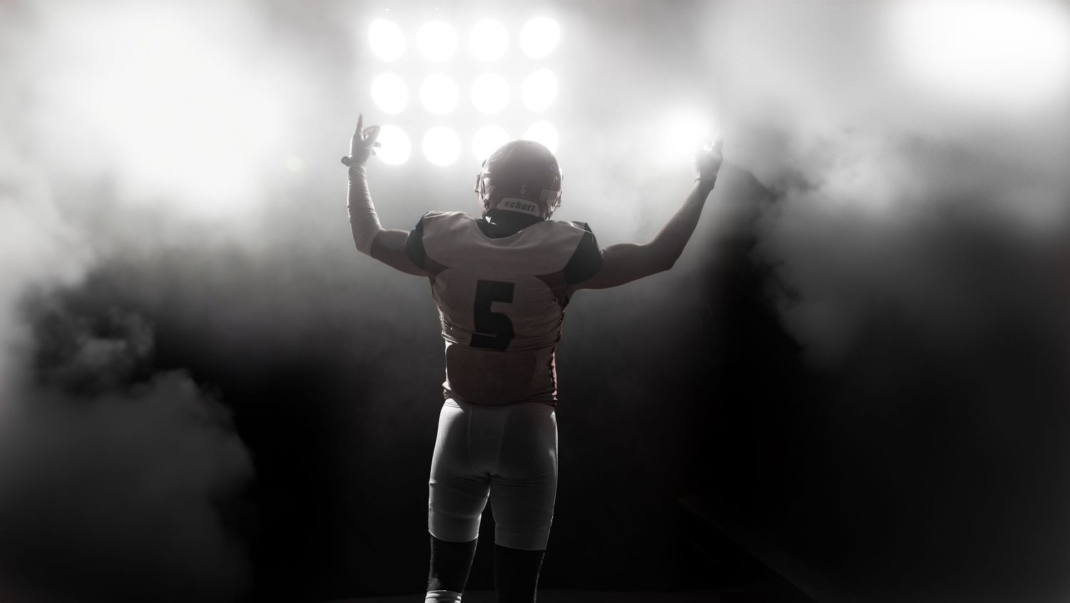 Silhouette of football player with raised arms in dramatic fog.