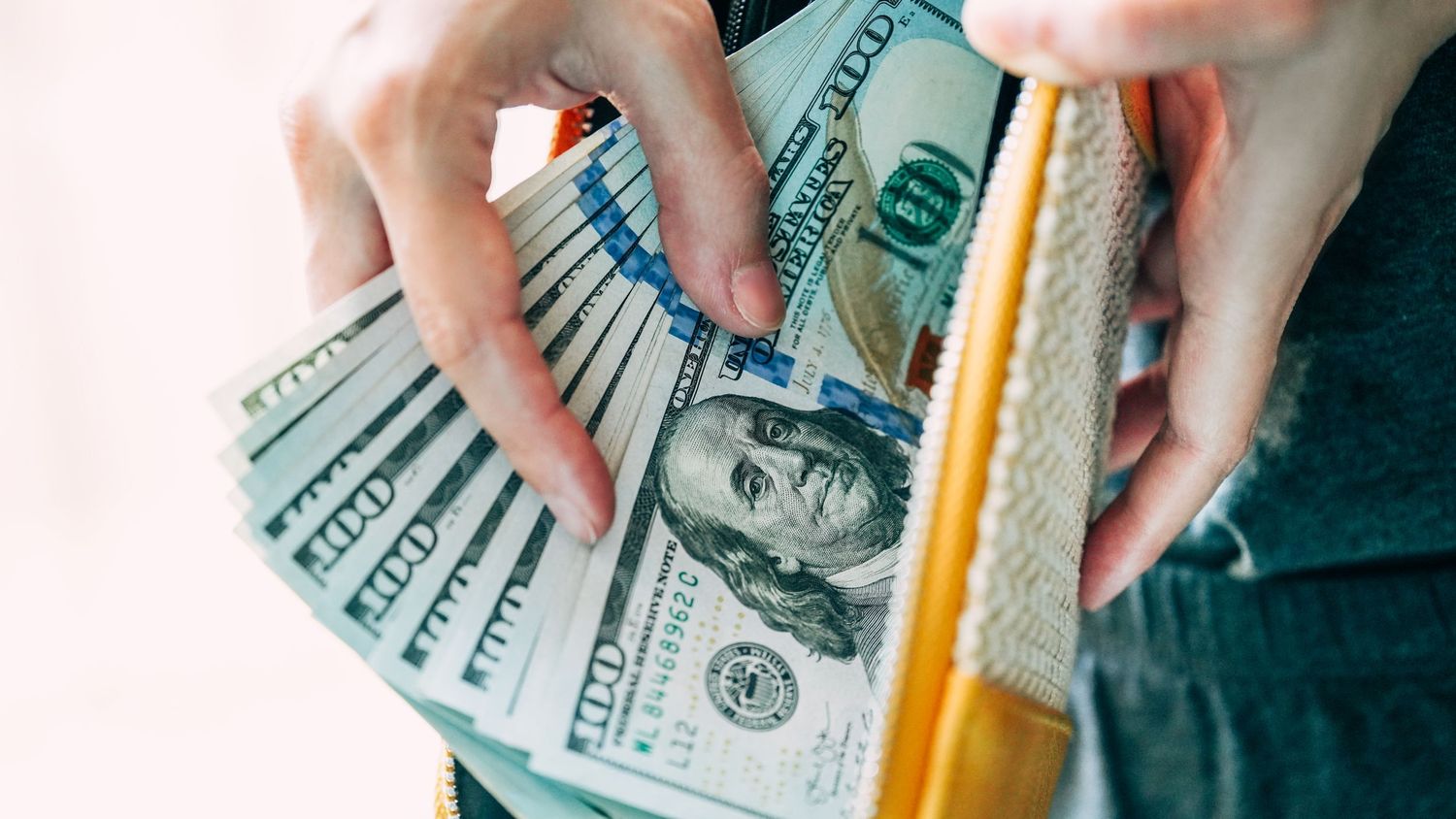 Hands counting and sorting through a stack of one hundred dollar bills spread out in a fan shape.