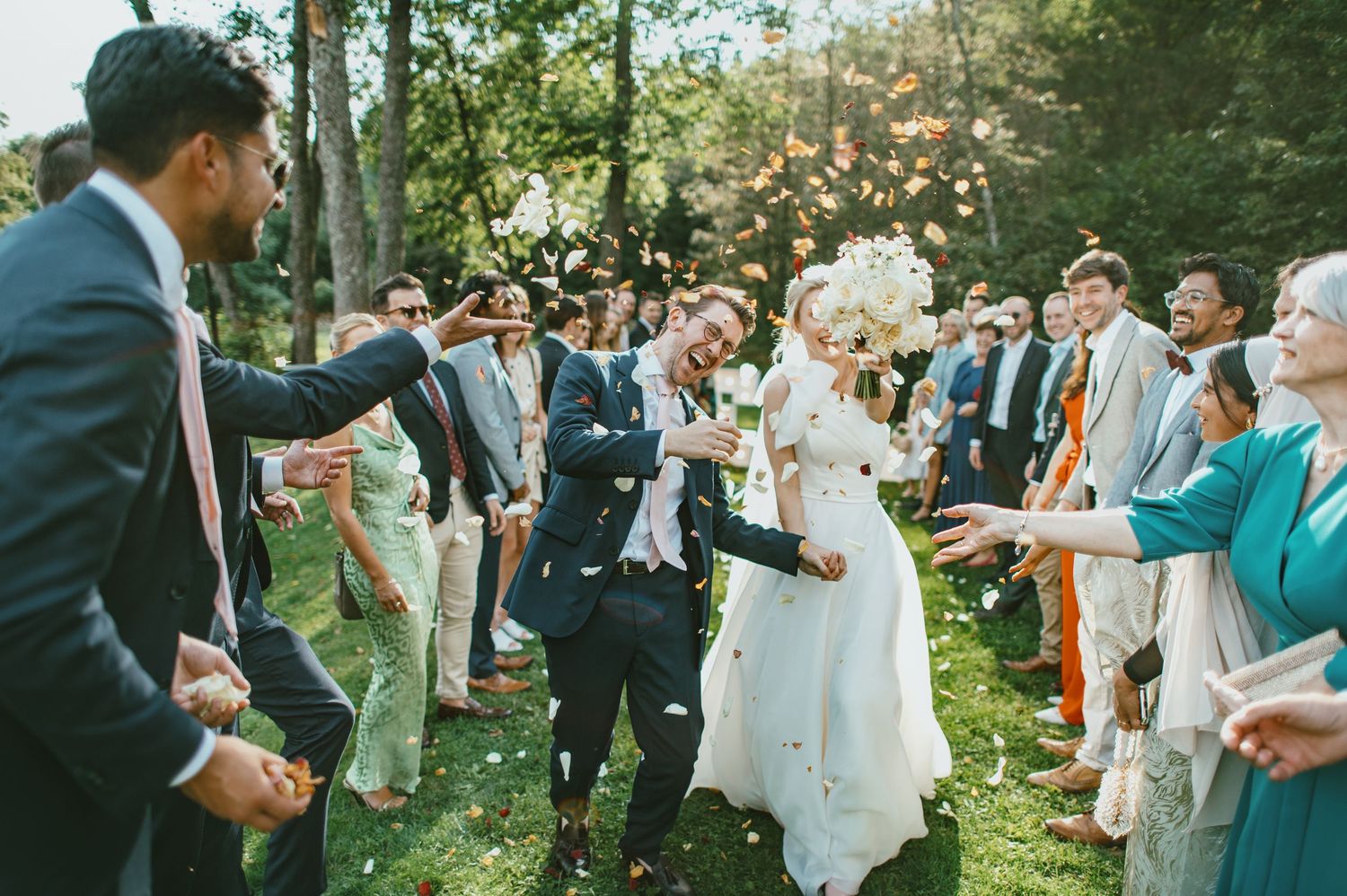 Wedding guests shower the newlyweds with flower petals during an outdoor garden celebration.