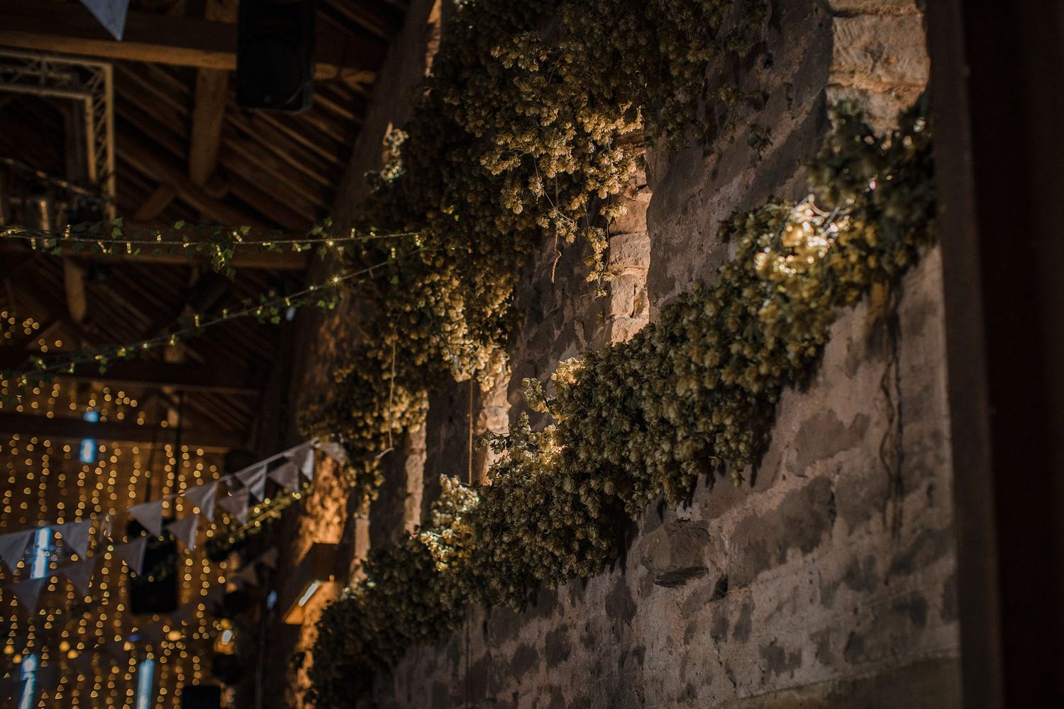 String lights and ivy adorn a rustic stone wall and wooden beam ceiling in evening lighting at Healy Events wedding venue in Kentville, NS.