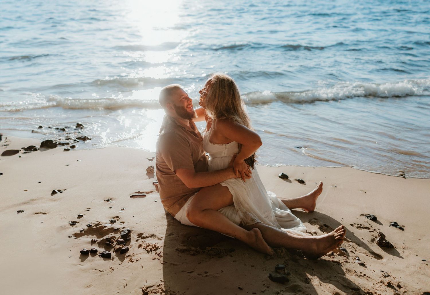 Romantic couple embracing on a sandy beach at sunset with gentle waves in the background.