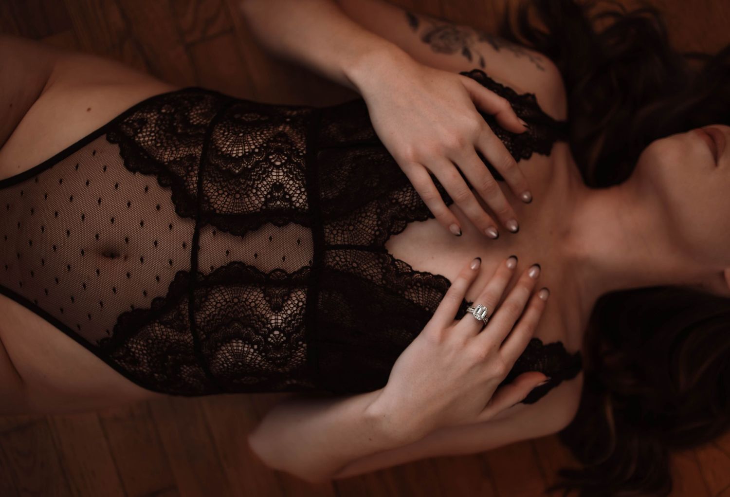 A moody close up photo of a woman in black lingerie laying on the floor with hands gently placed on her body capturing an intimate boudoir