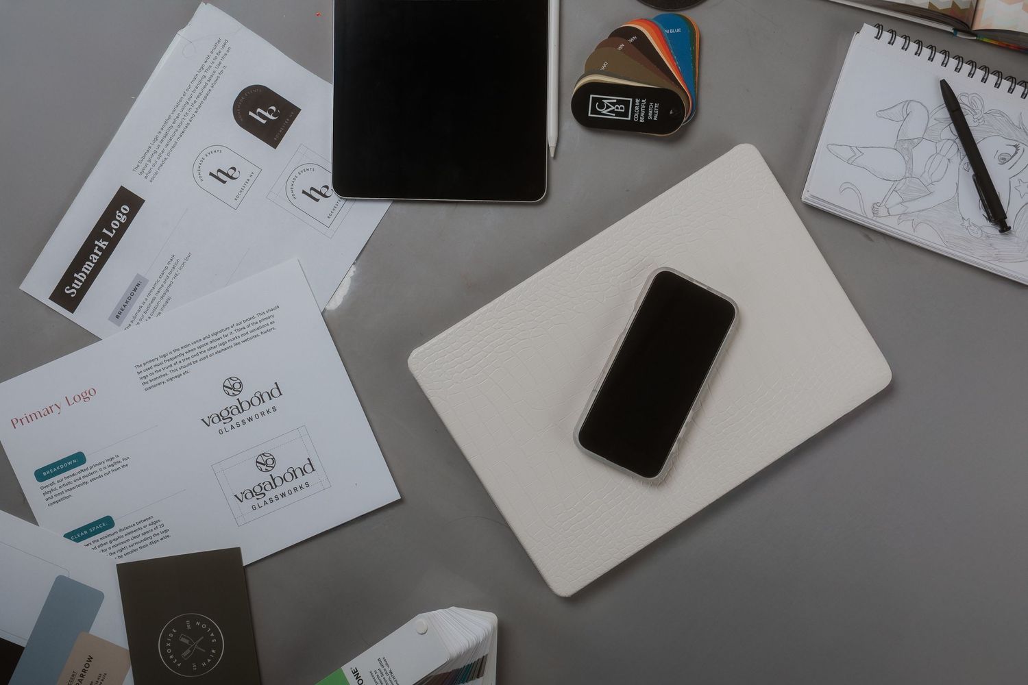 Flatlay of business stationery with smartphone, notebook and various papers on gray surface.