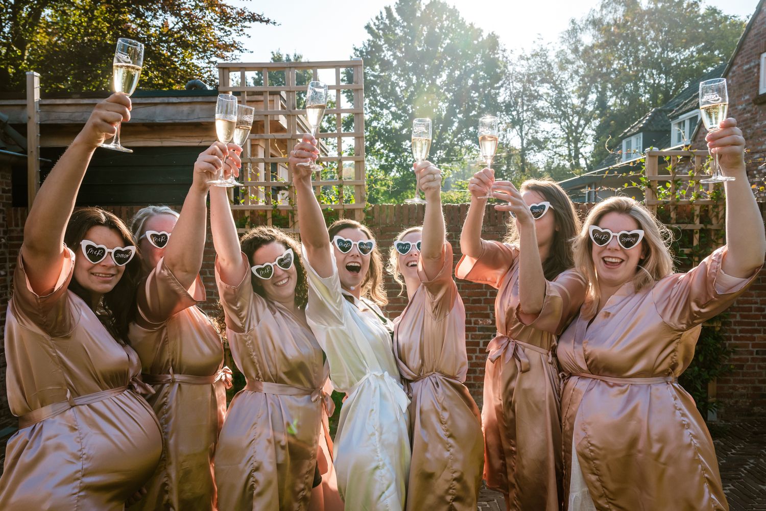 Bruidsmeisjes in satijnen jurken proosten met champagne, lachend en feestend met hartvormige brillen.