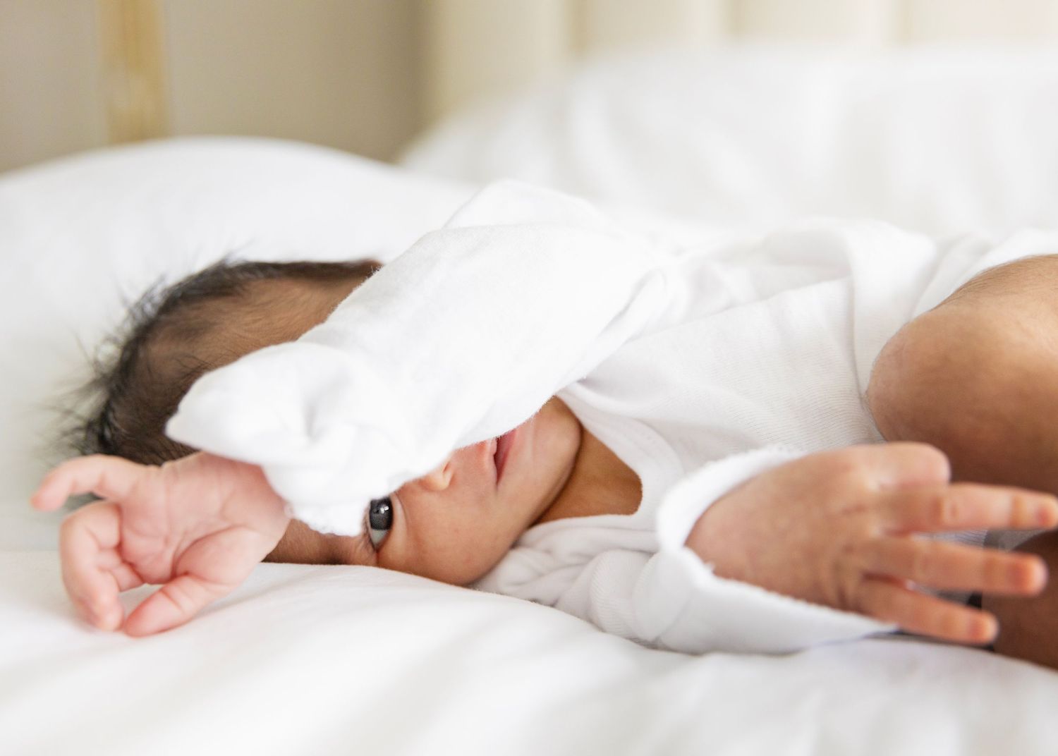 Person resting peacefully in white bedding while lying under soft white sheets.