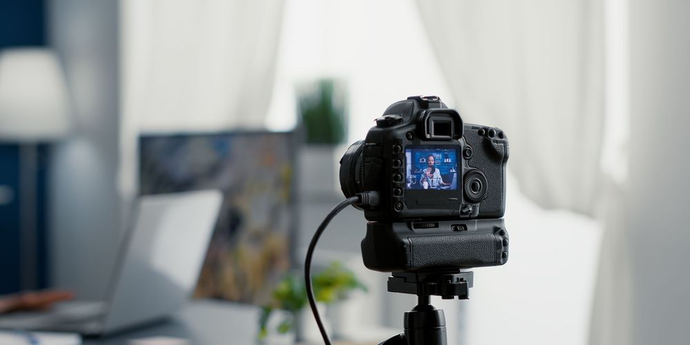 Professional DSLR camera mounted on a tripod in a home office setting, focused on a bright display screen.