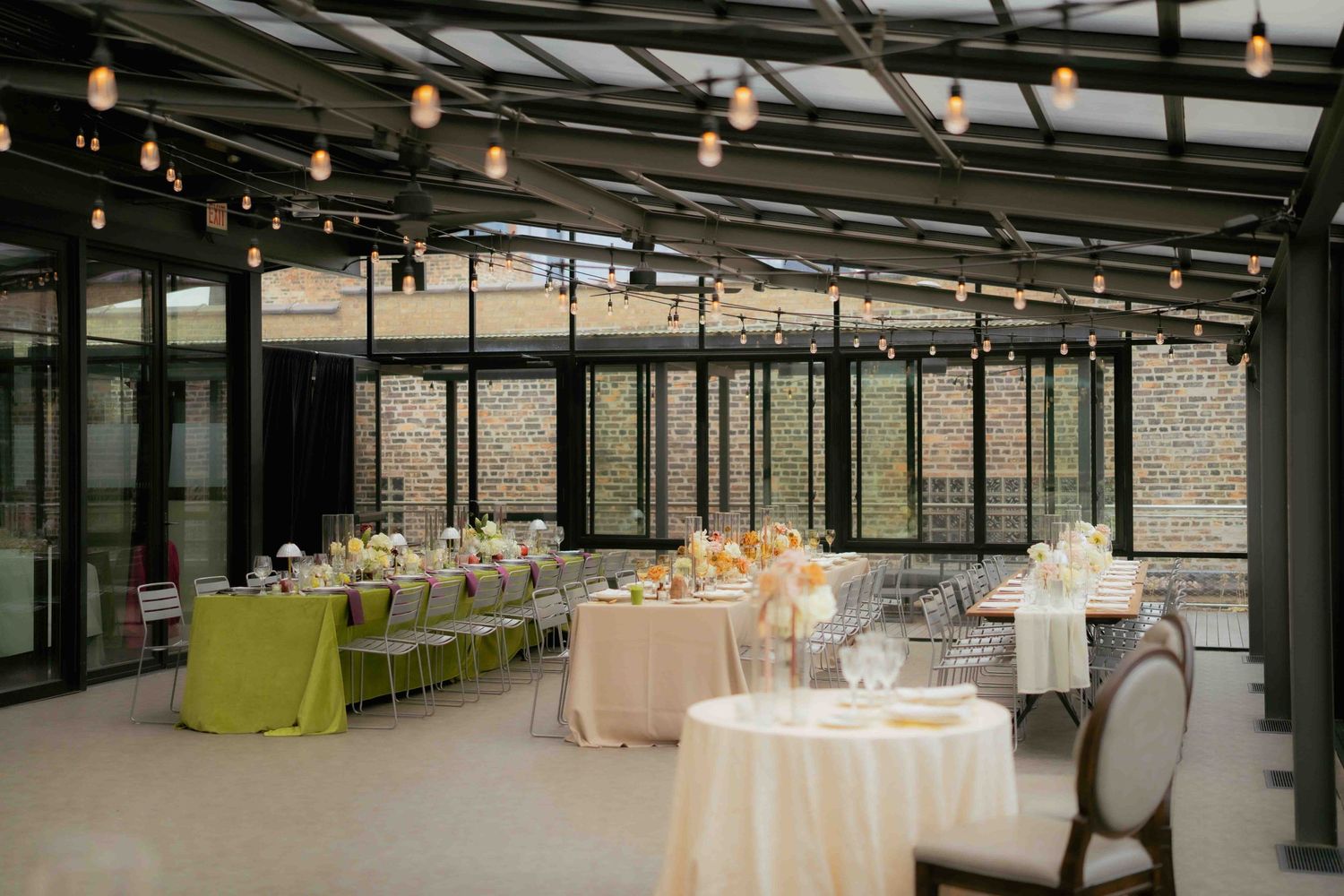 Modern event space with elegant table settings and string lights hanging from glass ceiling.