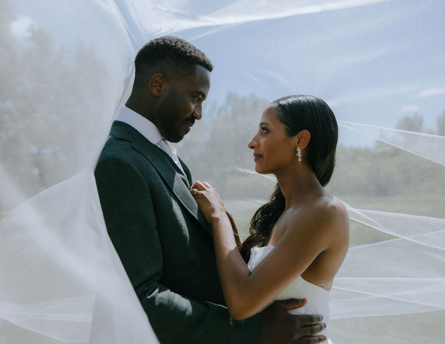 A couple shares an intimate moment together under a flowing white veil on their wedding day.