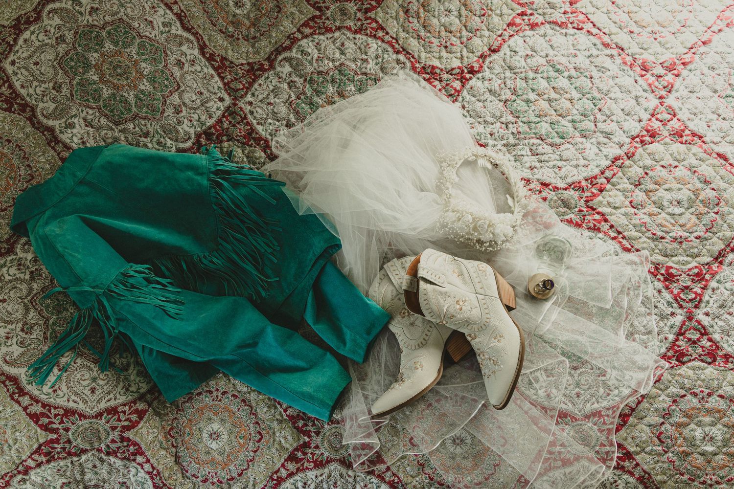 Wedding dress and emerald green dress laid out on patterned vintage carpet.