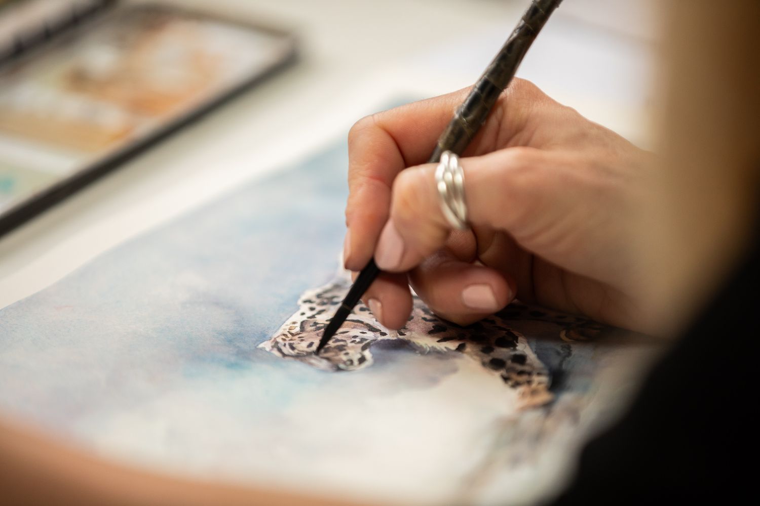 Close-up view of an artist's hand painting delicate details on a watercolor artwork with a fine brush.