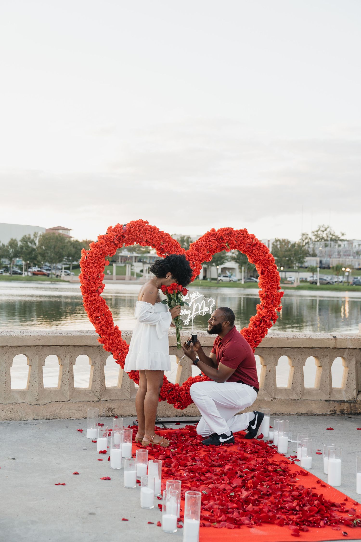 A newlywed couple relaxes on a green lawn in tropical garden setting with pink flowers and palm trees in background.