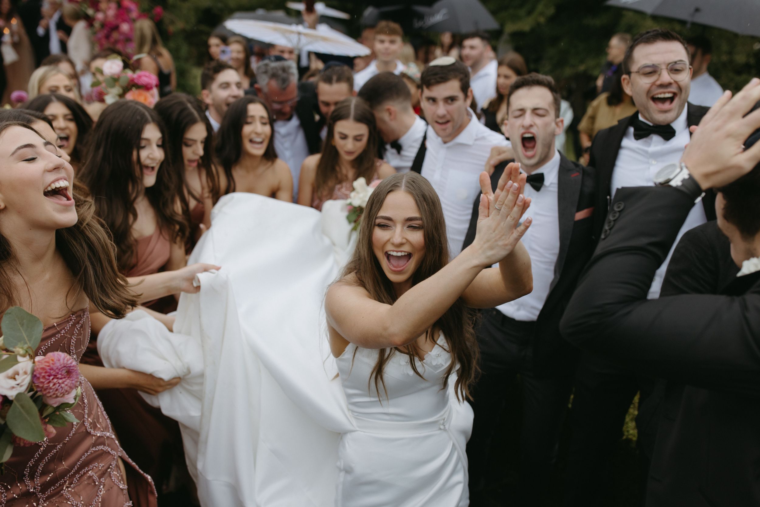 Wedding guests celebrate joyfully at an outdoor reception with pink floral decorations.