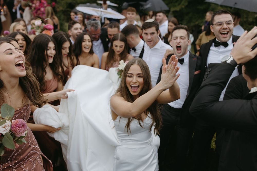Wedding guests celebrate joyfully at an outdoor reception with pink floral decorations.