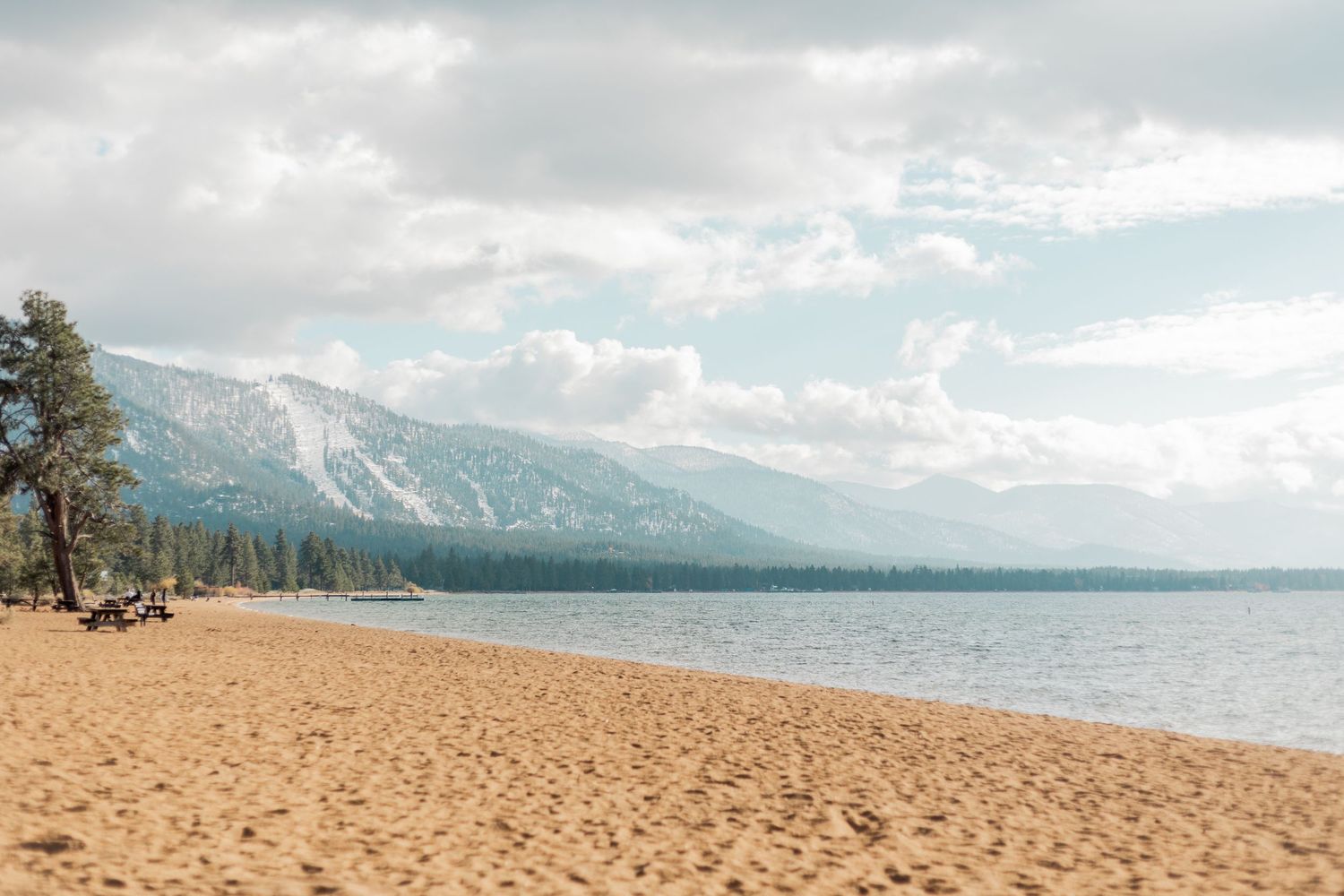 A scenic beach landscape with mountains and Lake Tahoe in the background.