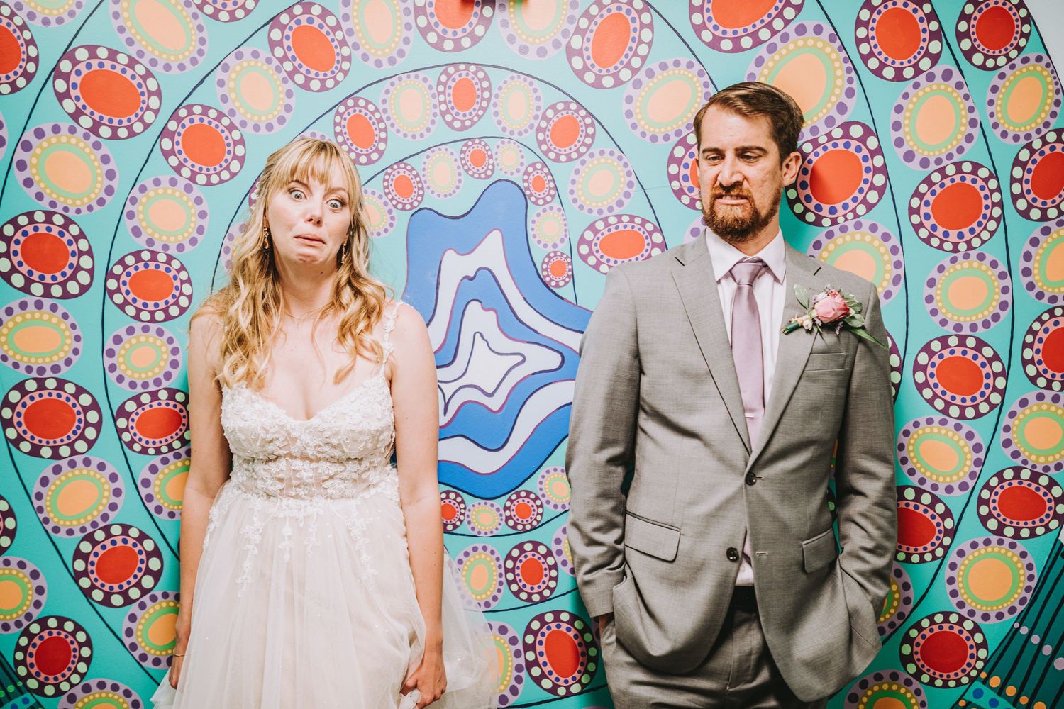 Bride and groom posing seriously in front of vibrant colorful psychedelic mural backdrop at wedding.