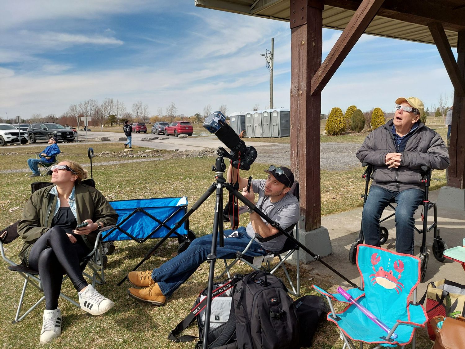 Group of people with telescopes and equipment gathered under a wooden shelter.