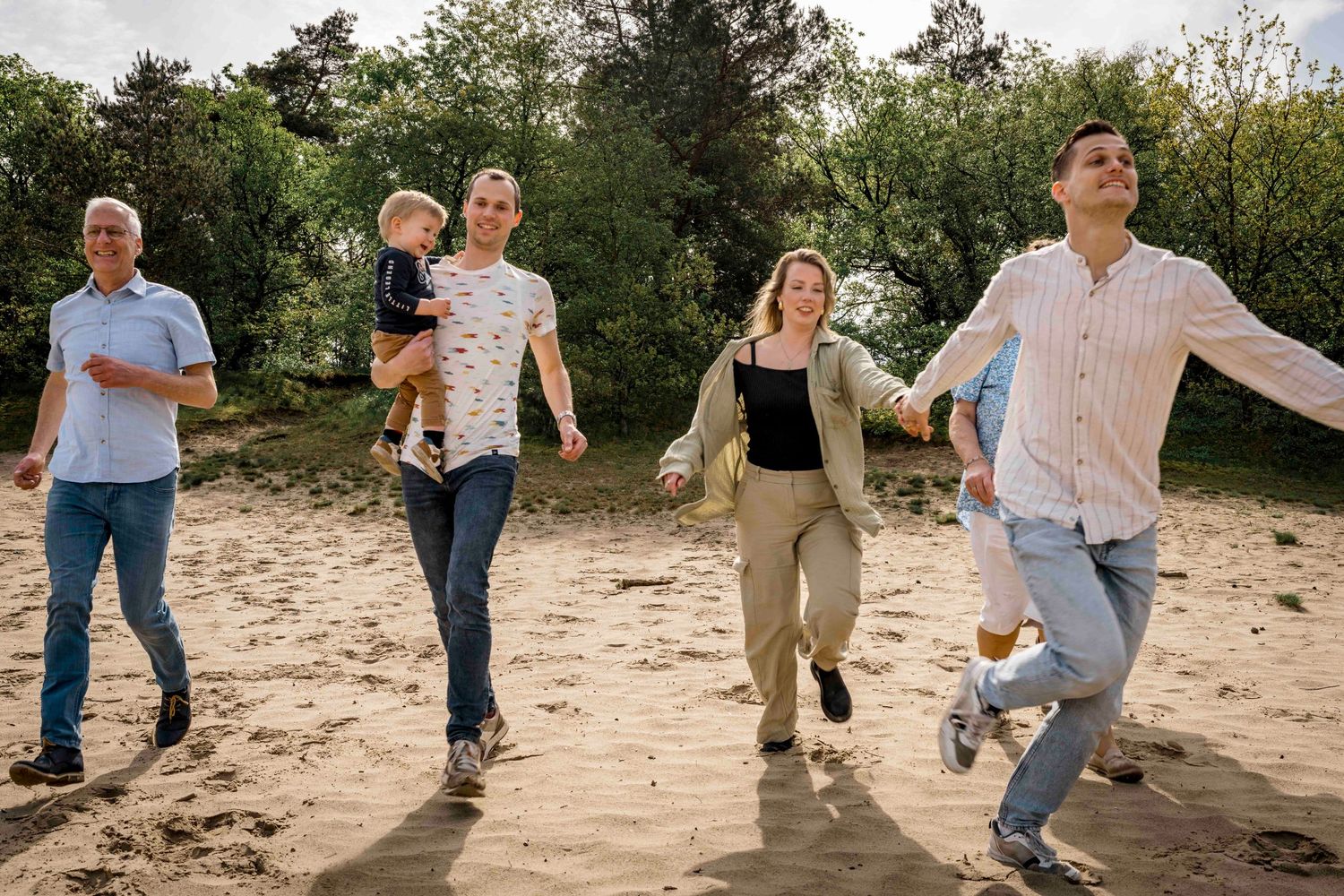 Group enjoying a playful walk together on sandy terrain surrounded by trees.