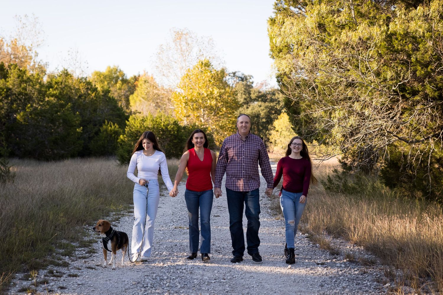 A group walks together with their pet dog along a gravel path through autumn scenery.